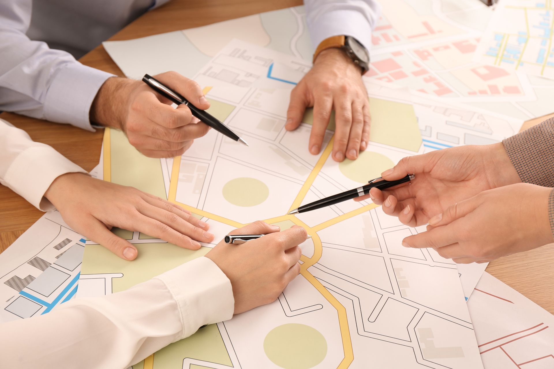 Hands of three professional cartographers working with a cadastral map on a table.
