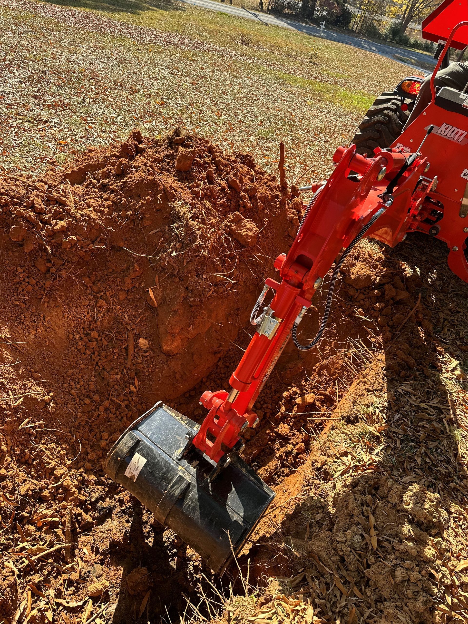 A Red Kubota Tractor Is Digging A Hole In The Dirt - Clemmons, NC - Jetco Septic Service
