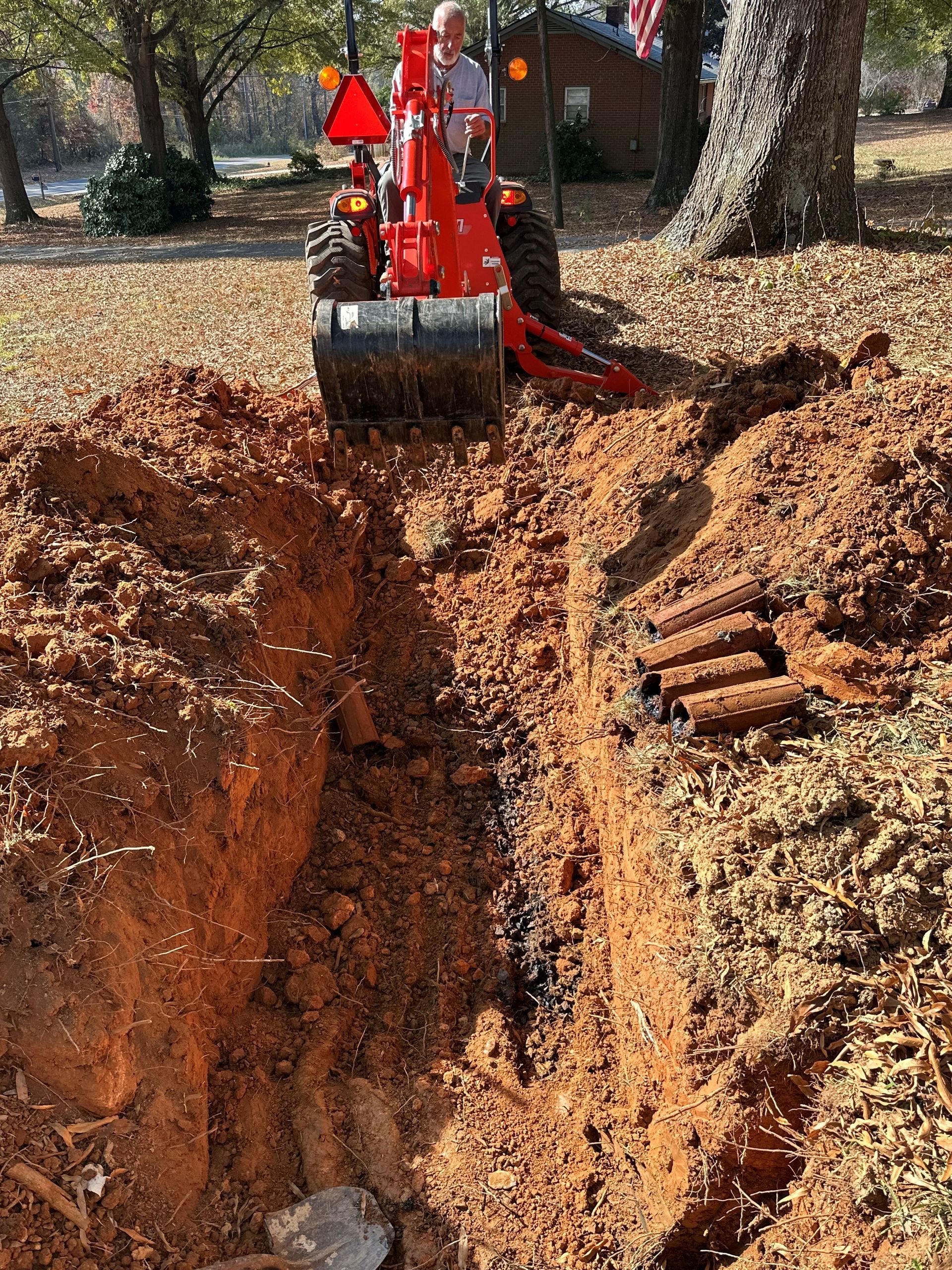 A Man Is Driving A Red Tractor In A Dirt Field - Clemmons, NC - Jetco Septic Service