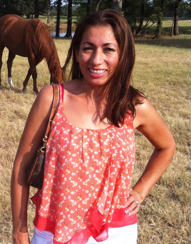A woman stands in a field with a horse in the background
