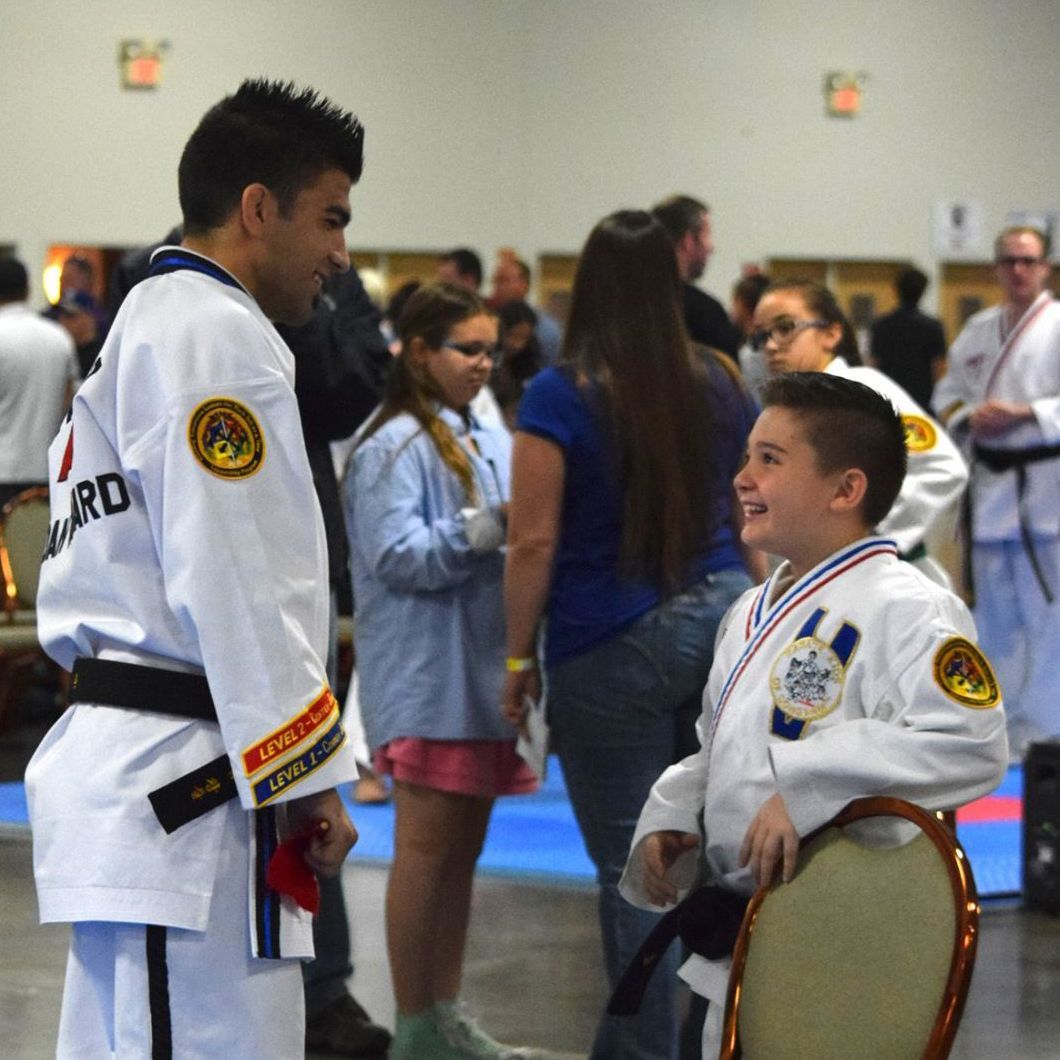 A man in a taekwondo uniform is talking to a young boy