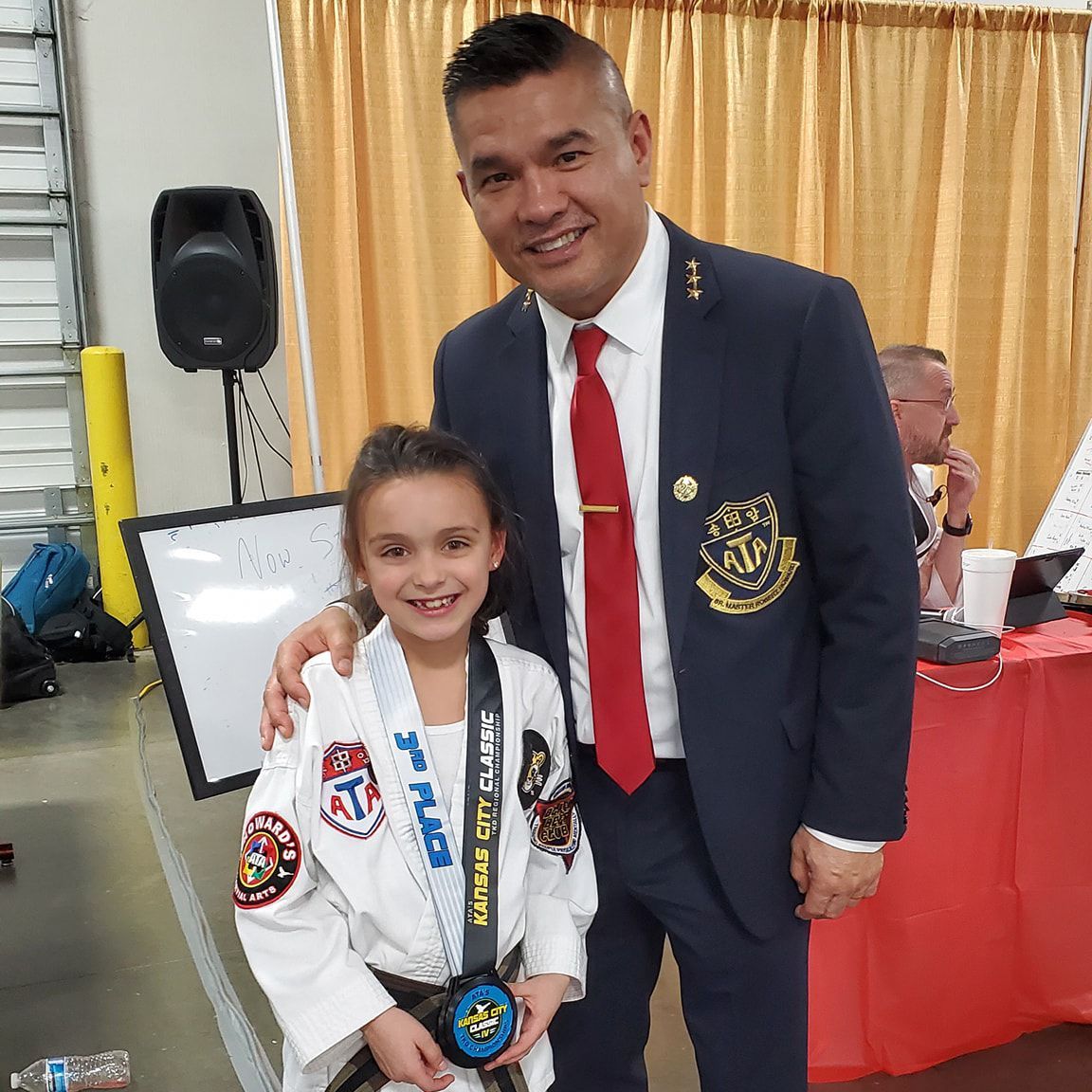 A man in a suit and tie is posing for a picture with a young girl in a karate uniform.