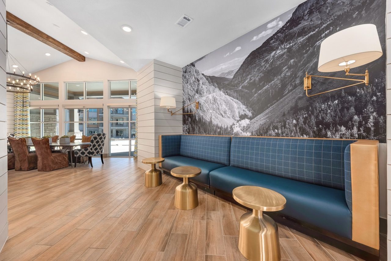 Lounge area with blue bench seating, gold tables, mountain mural on wall, and glass doors.