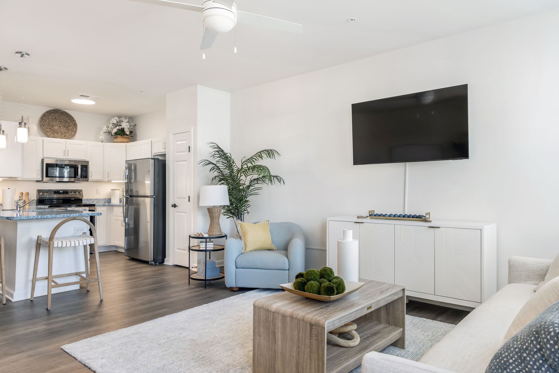Bright modern living room with kitchen, TV, blue chair, and white couch.