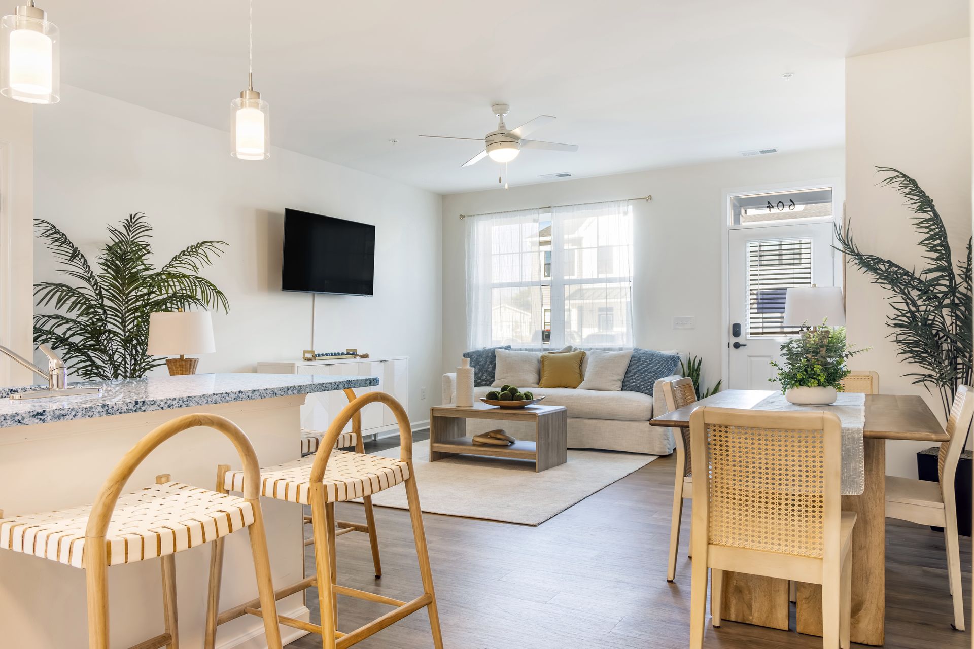 Brightly lit modern living space with kitchen island, seating, sofa, and dining area.