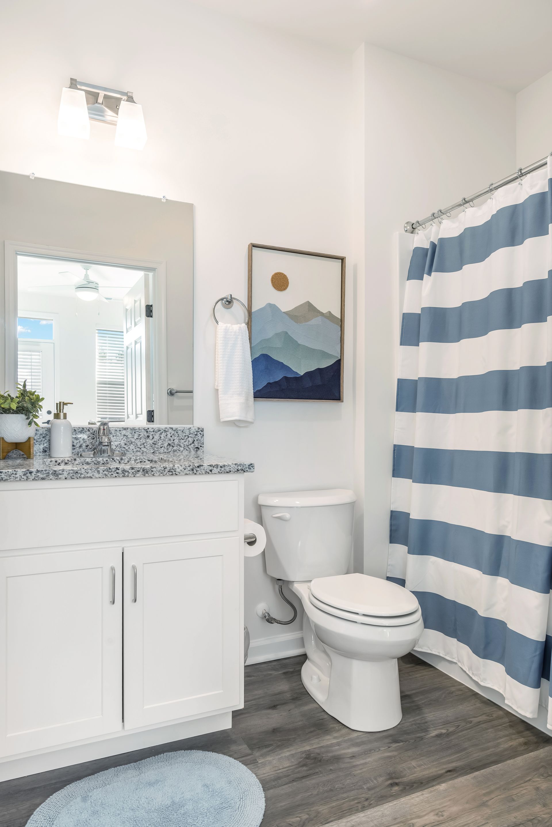 Bathroom with white cabinetry, blue accents, gray flooring, and a striped shower curtain.