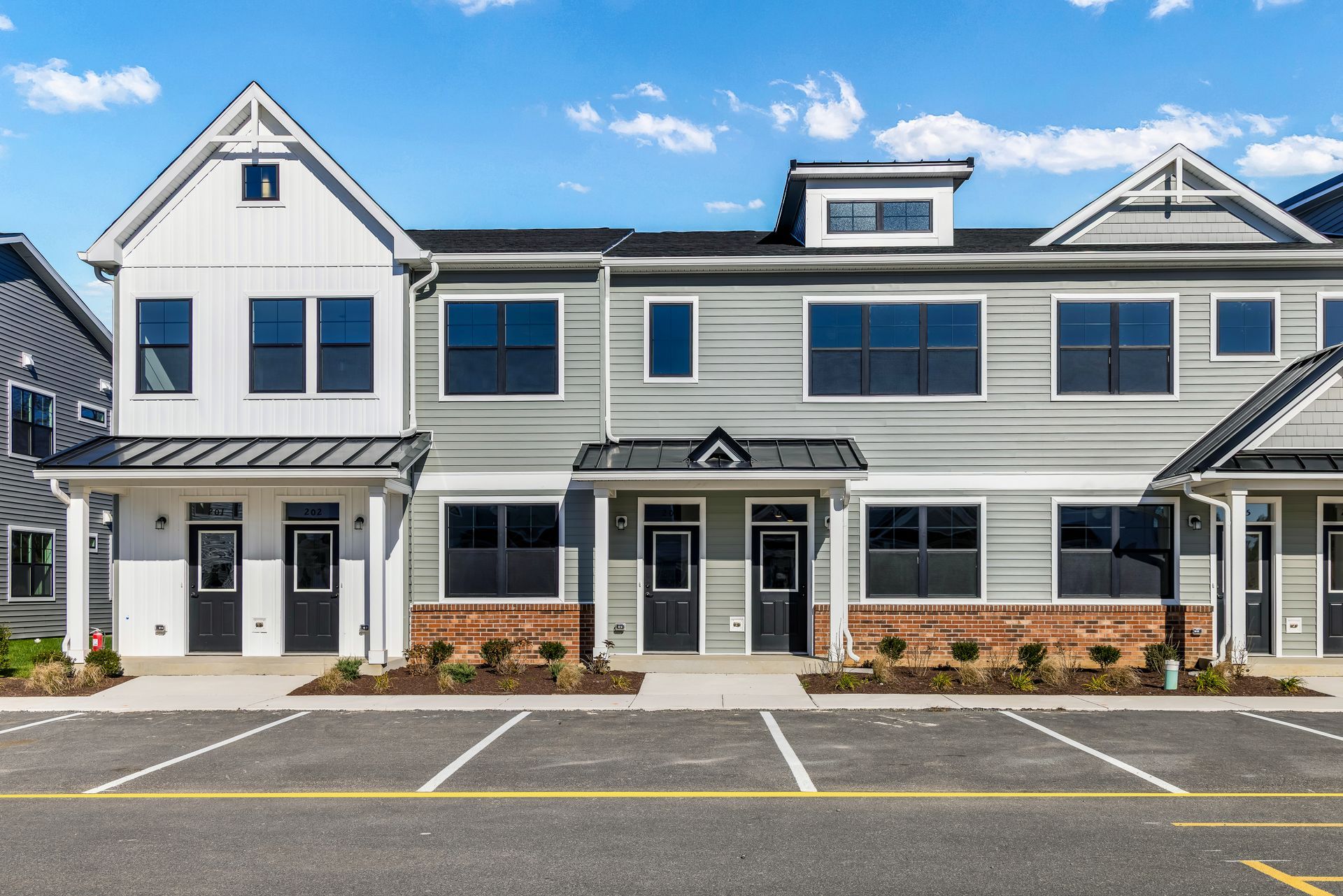 Row of modern townhomes with gray siding, dark doors, and a parking lot.