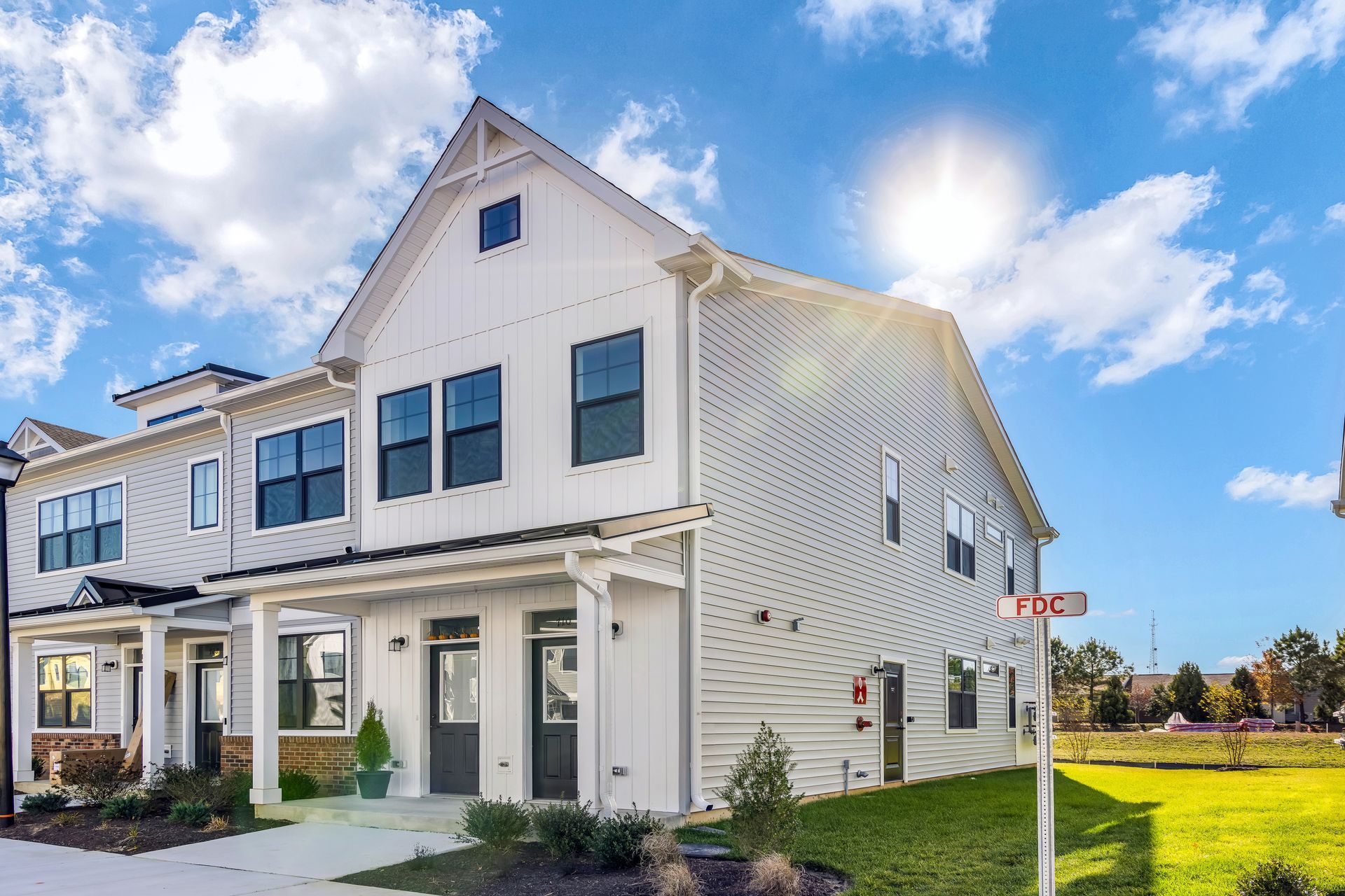 White townhouses under a bright sunny sky; green lawn, small sign.