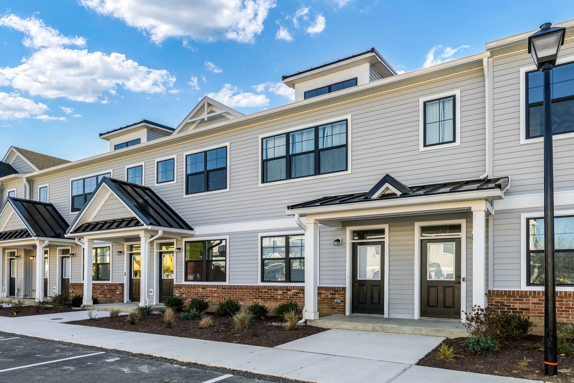 Exterior of light grey townhouses with black trim and doors under a blue sky.