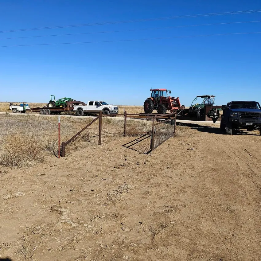 Dirt road with farm vehicles: tractor, truck, and trailer under a blue sky.