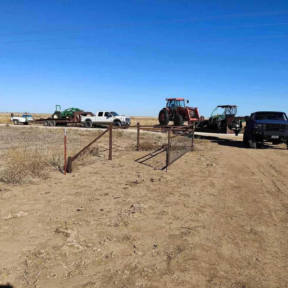 Dirt road with farm vehicles: tractor, truck, and trailer under a blue sky.