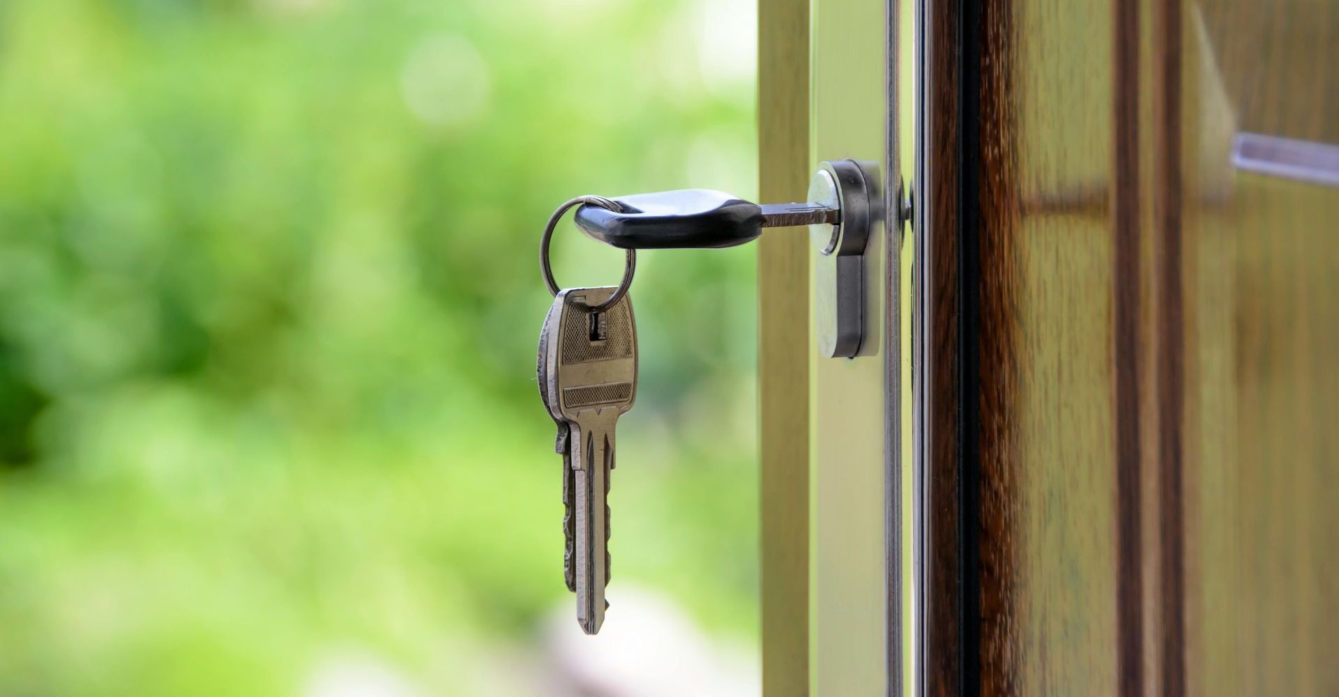 Keys in a door lock, with a green, blurred background.