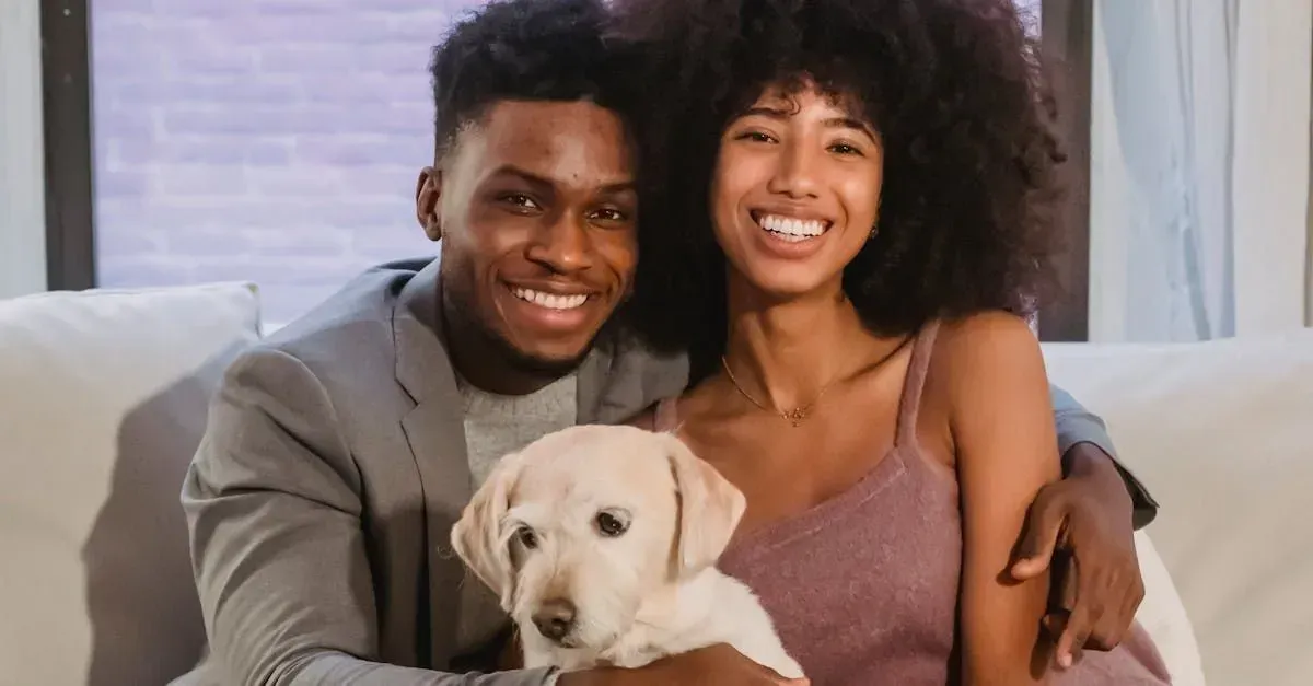 A smiling couple with a light-colored dog sits on a couch. The man wears a blazer, the woman a dress.