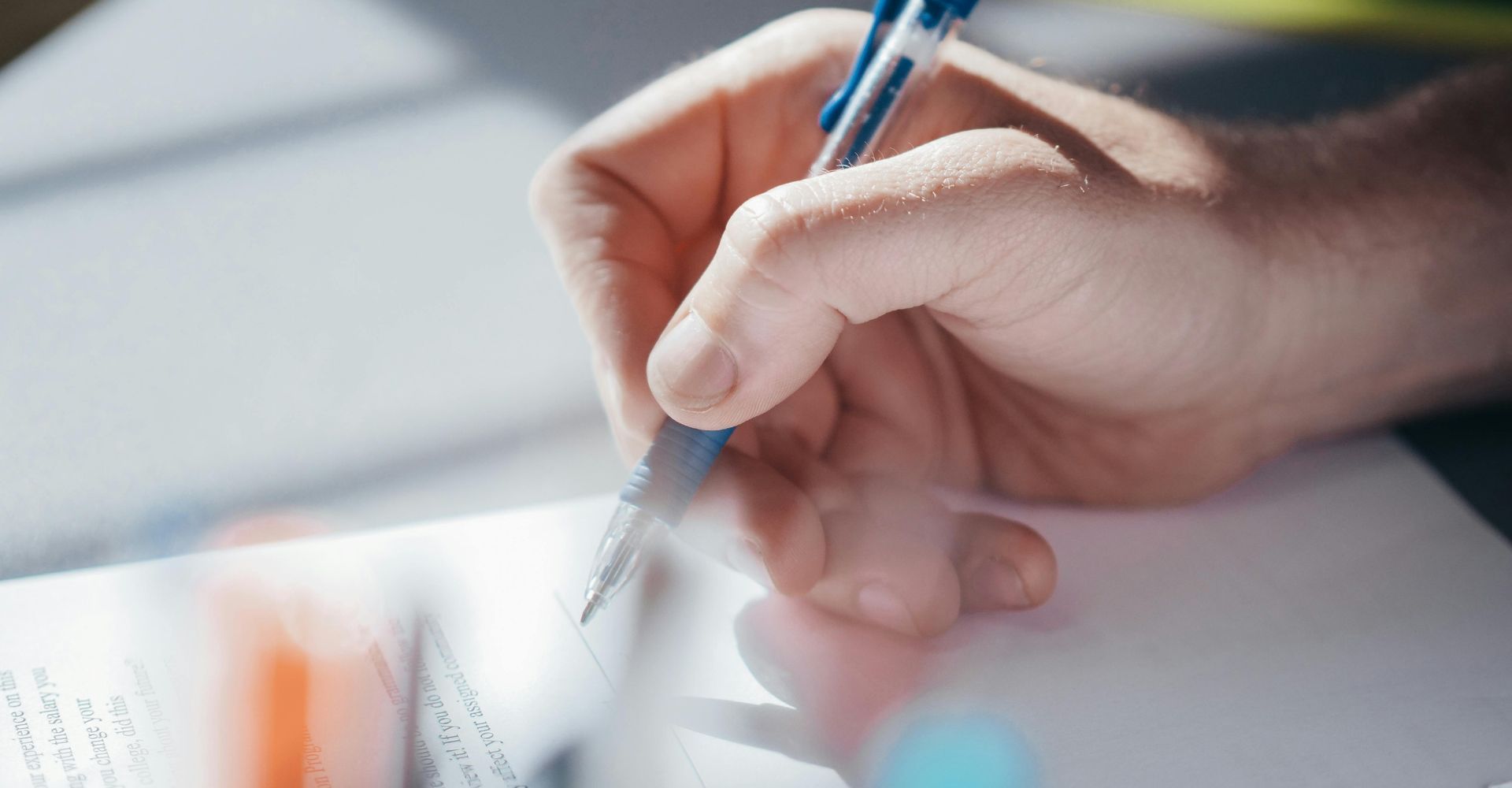 Person's hand writing with a blue pen on a white paper.