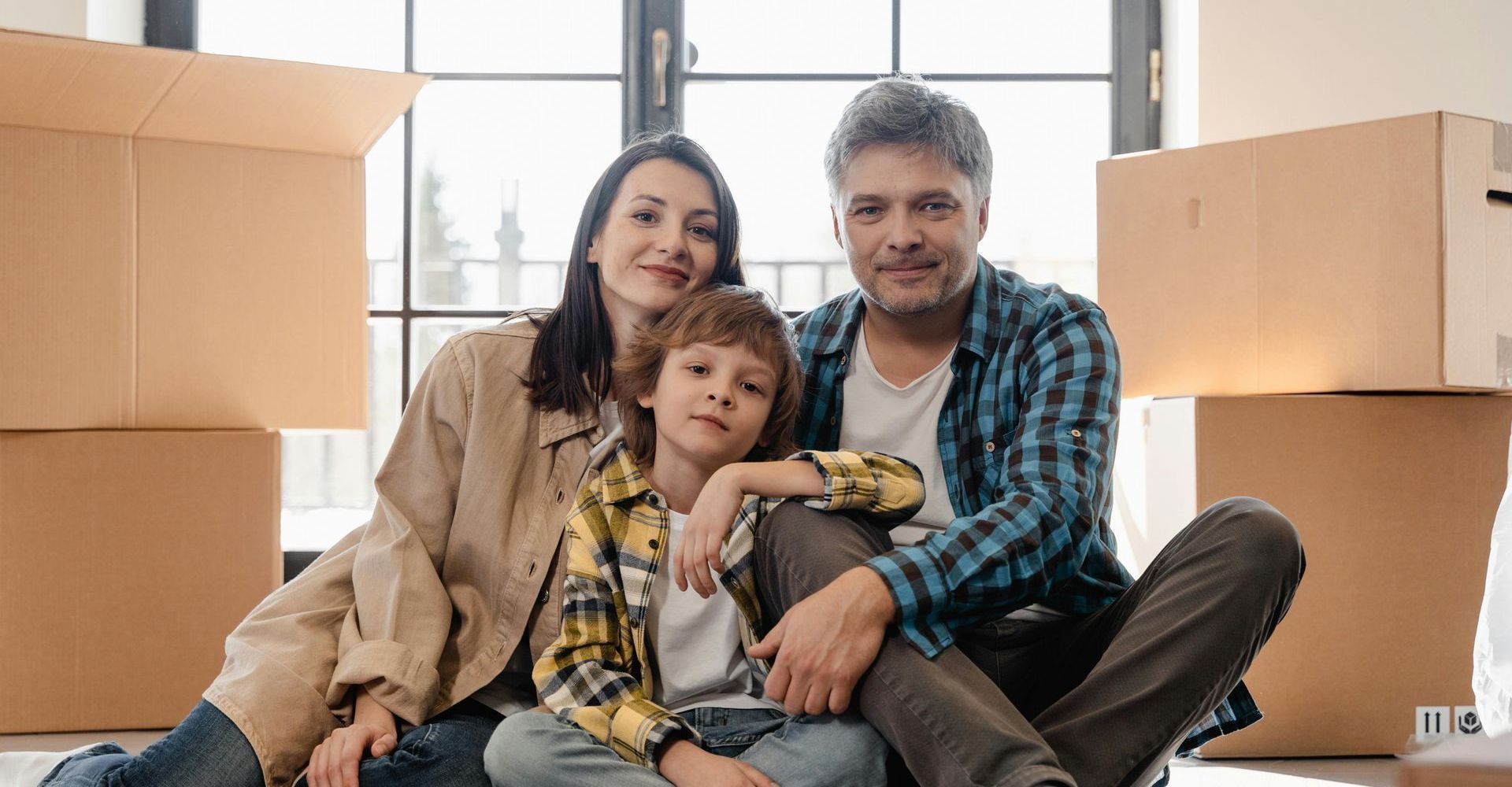 Family of three smiling, sitting among moving boxes in new home.