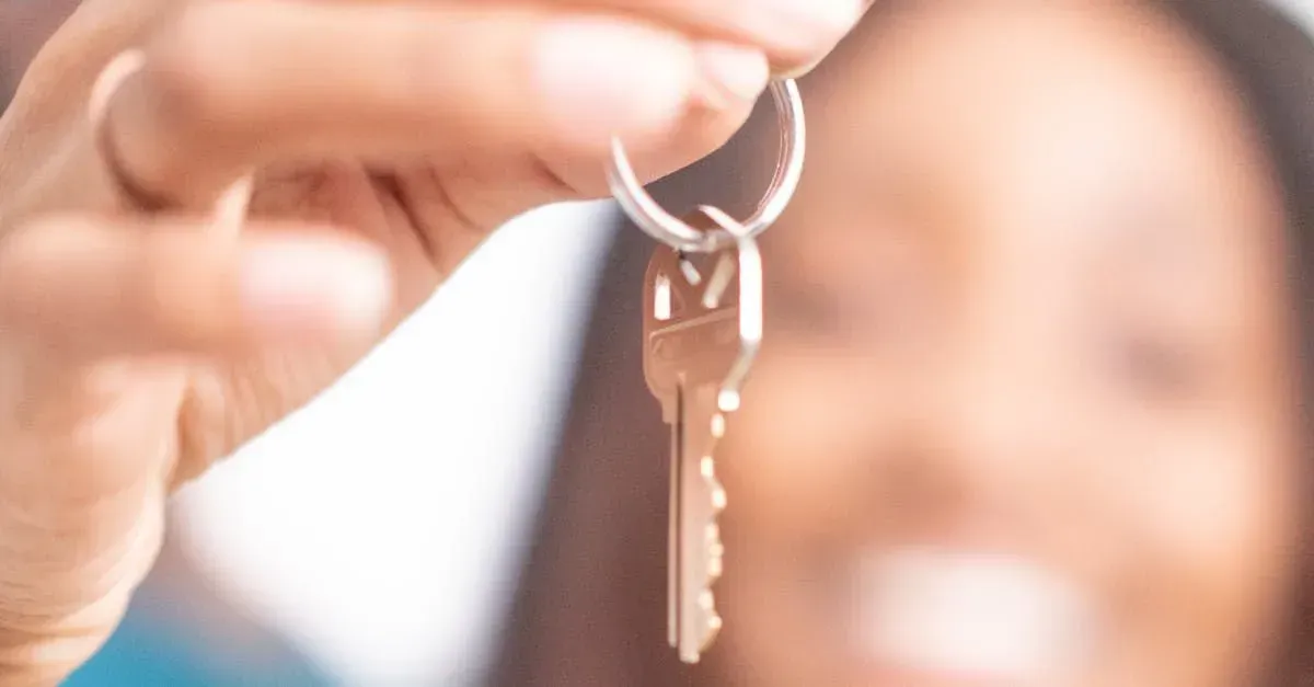 Person holding up a house key, smiling, blurry background.