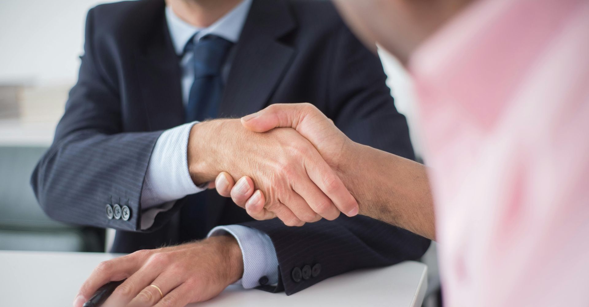Two men in business attire shaking hands at a table.
