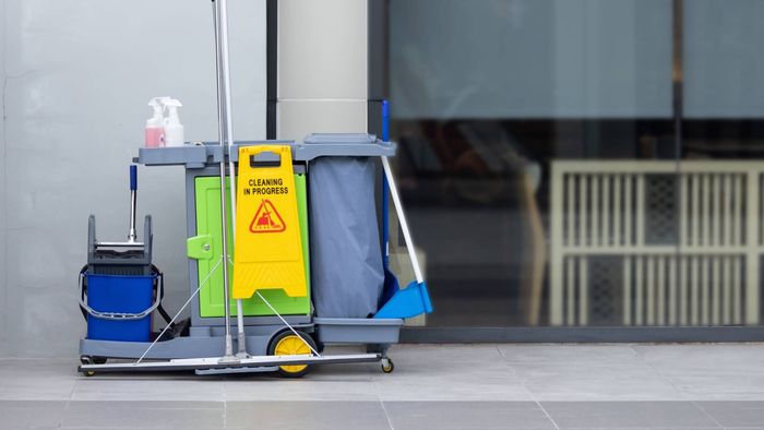 A cleaning cart with a yellow caution sign on it is parked in front of a building.