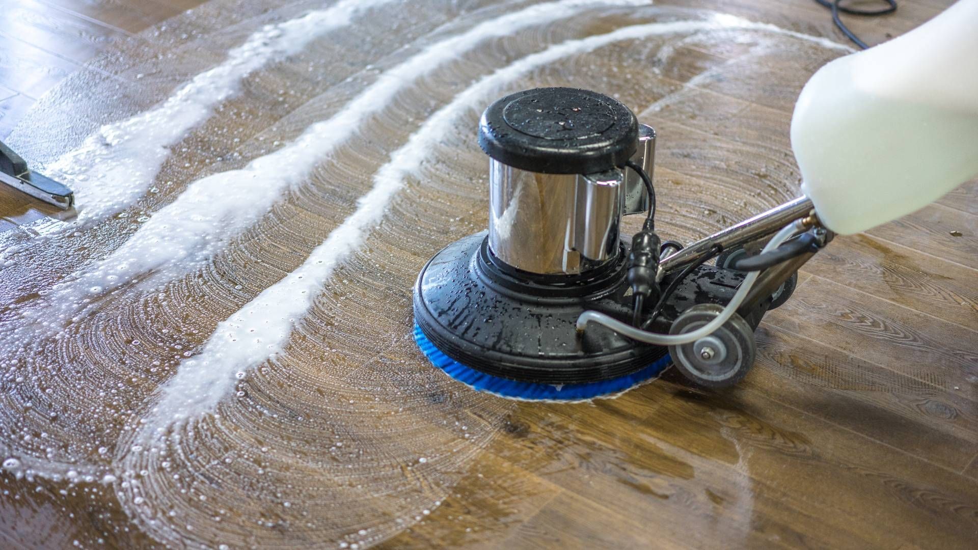 A person is using a machine to clean a wooden floor.