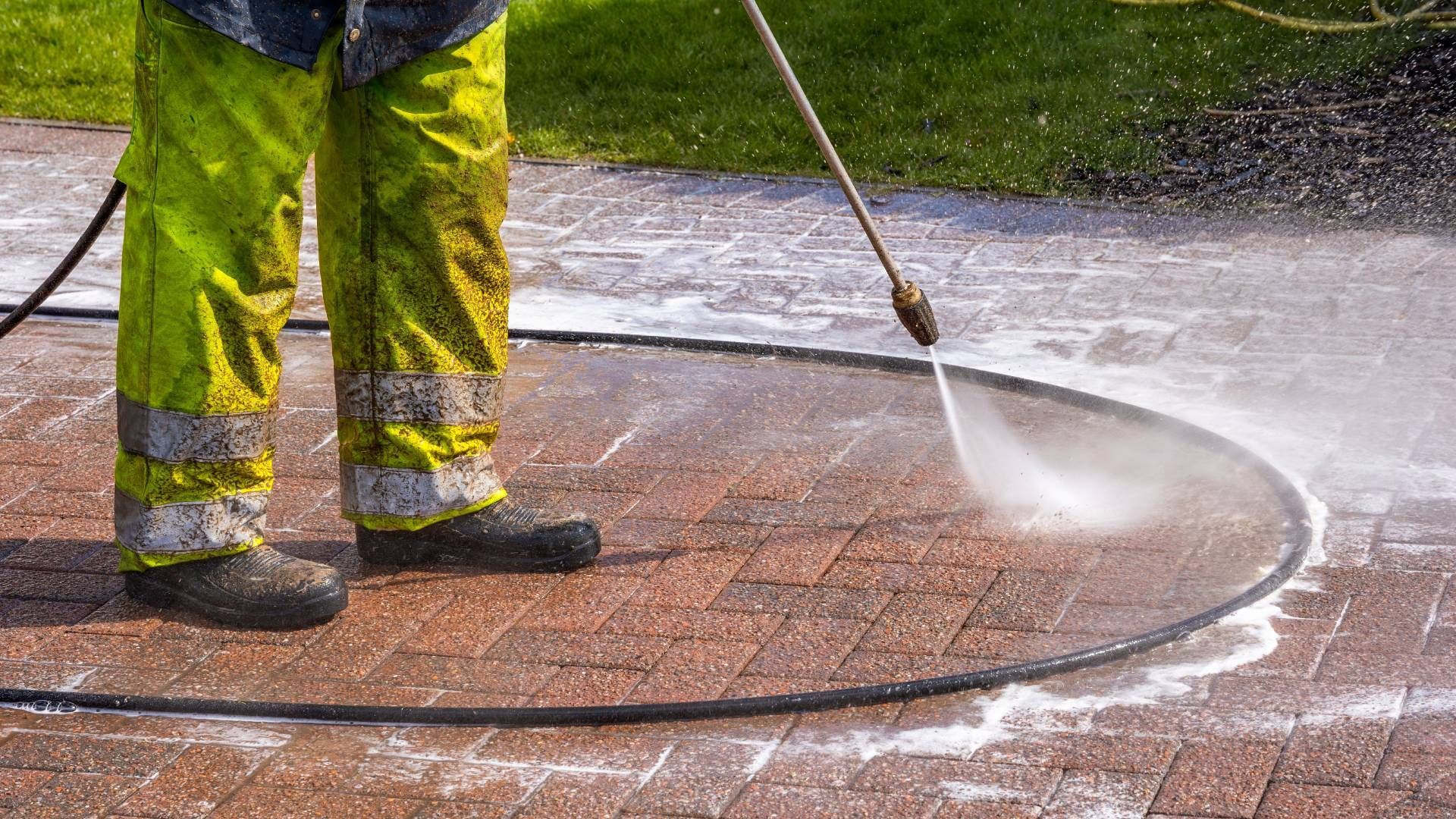 A man is using a high pressure washer to clean a brick walkway.