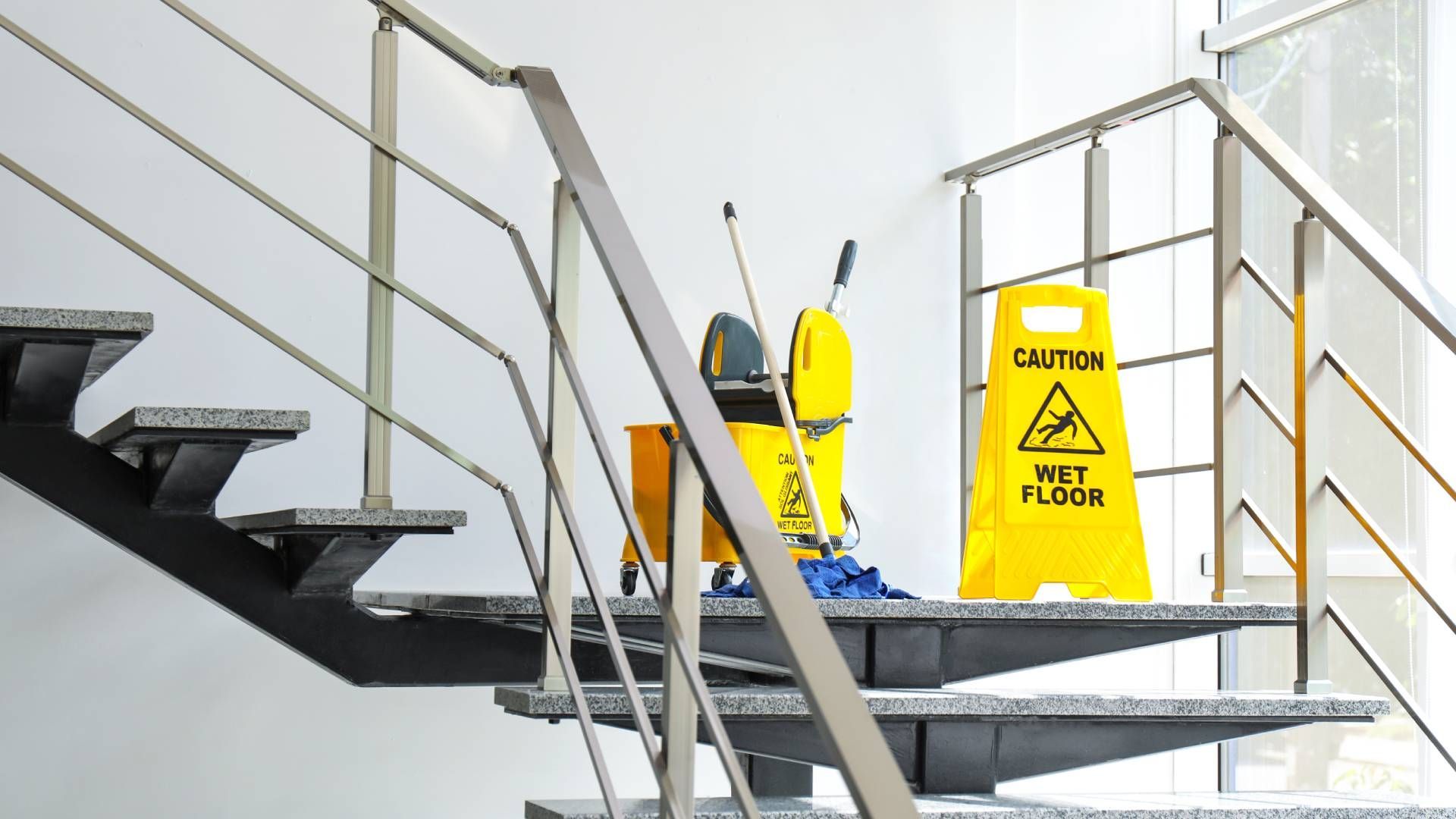 A caution wet floor sign is on the stairs next to a mop and bucket.