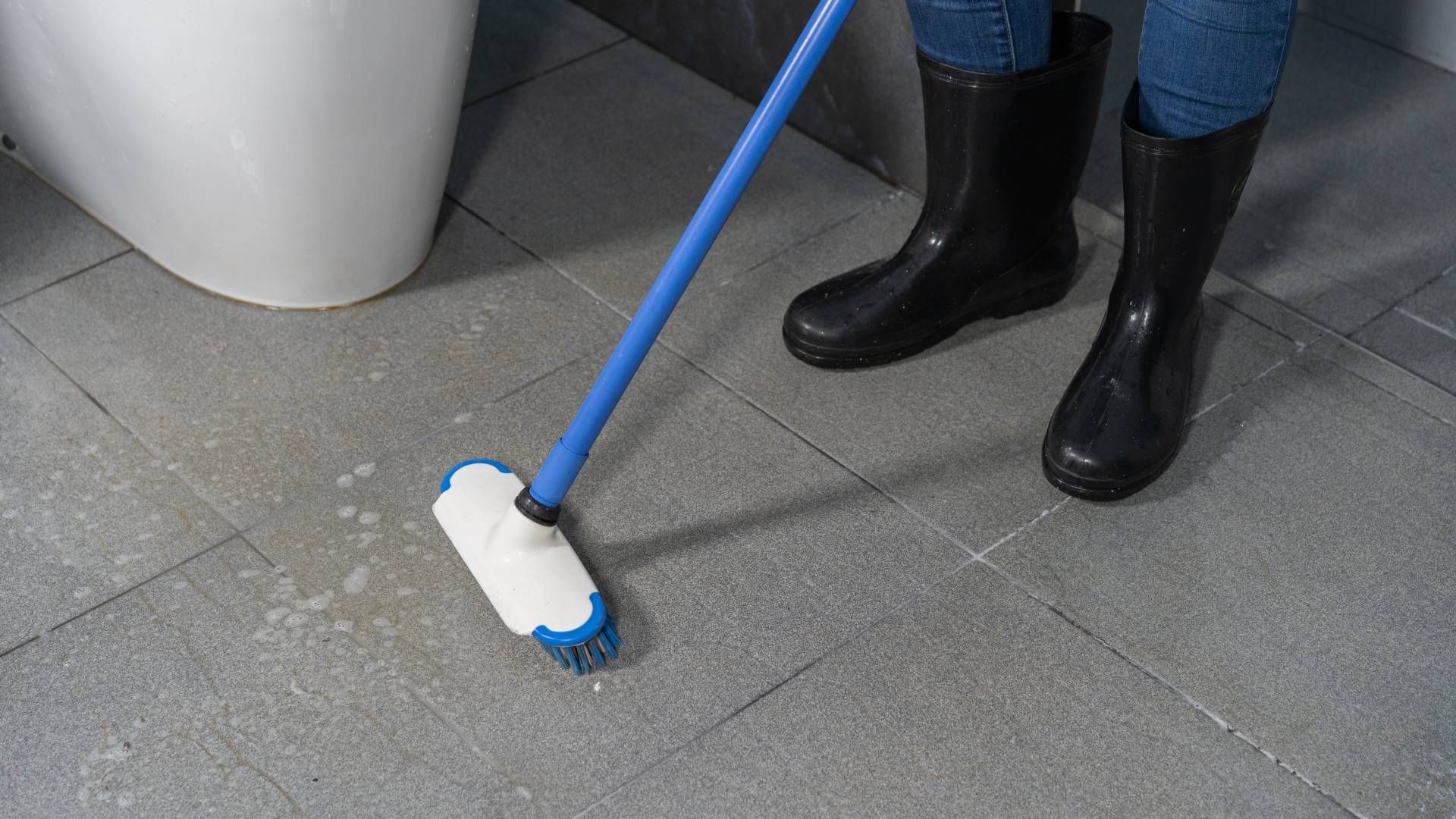 A person is cleaning the floor of a bathroom with a broom.