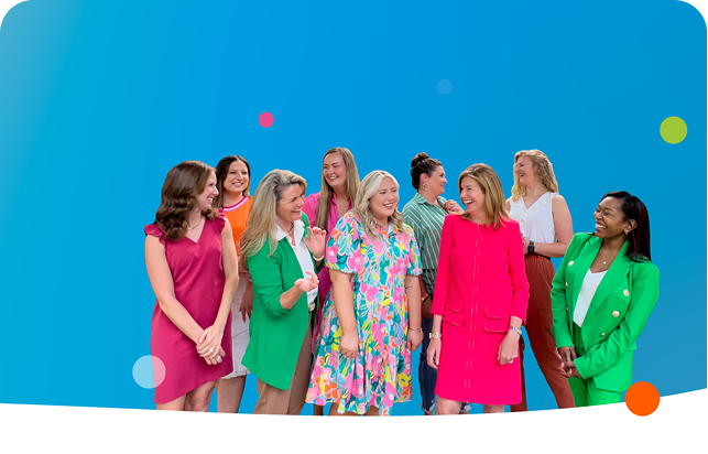 Group of women in colorful outfits smiling against a blue backdrop.