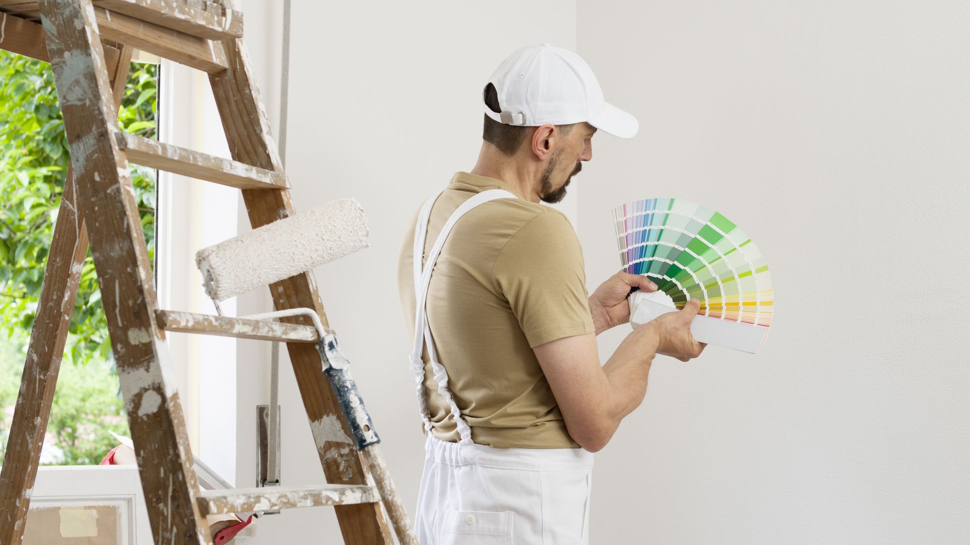 A man is standing next to a ladder holding a palette of paint.