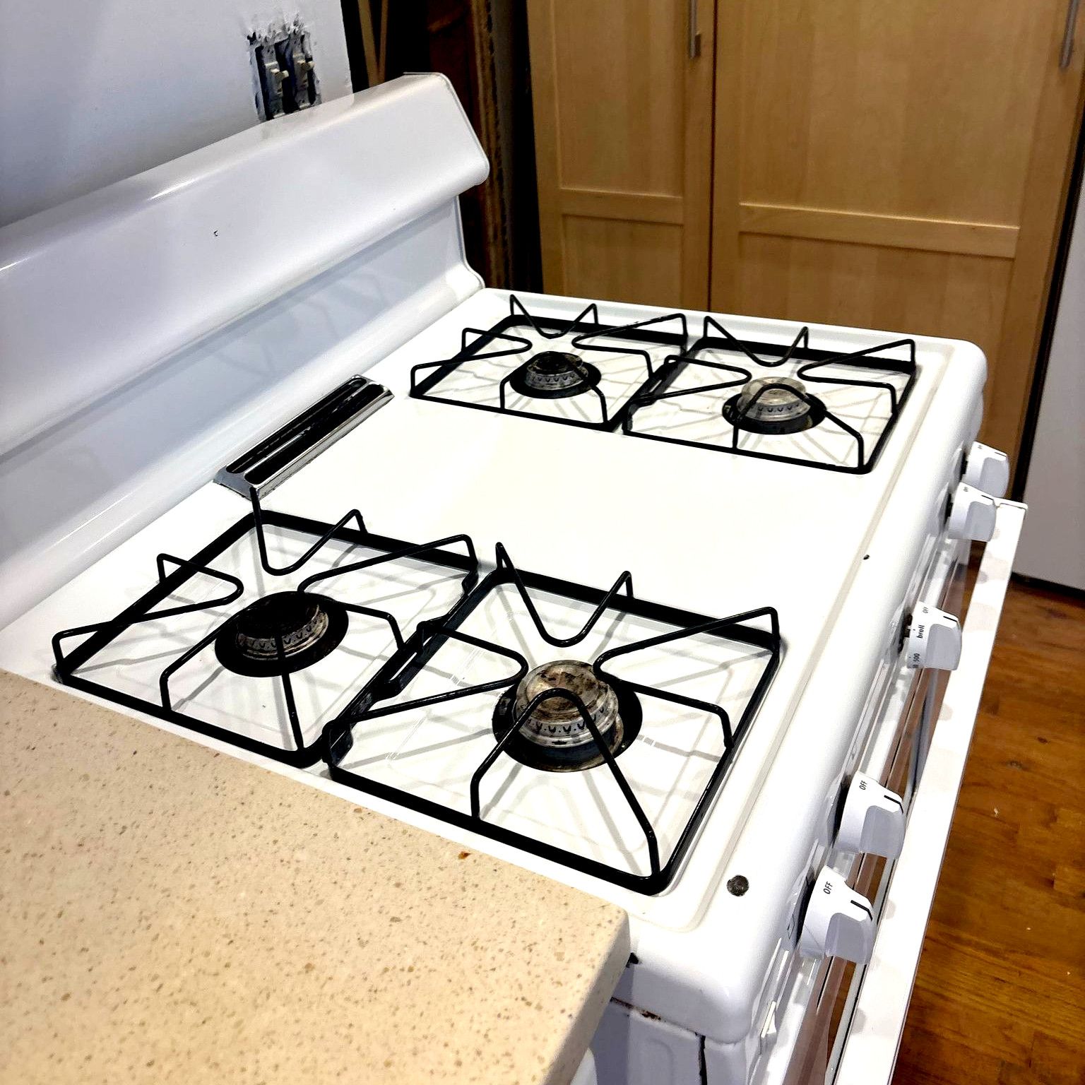A white gas stove with four burners is sitting on a counter