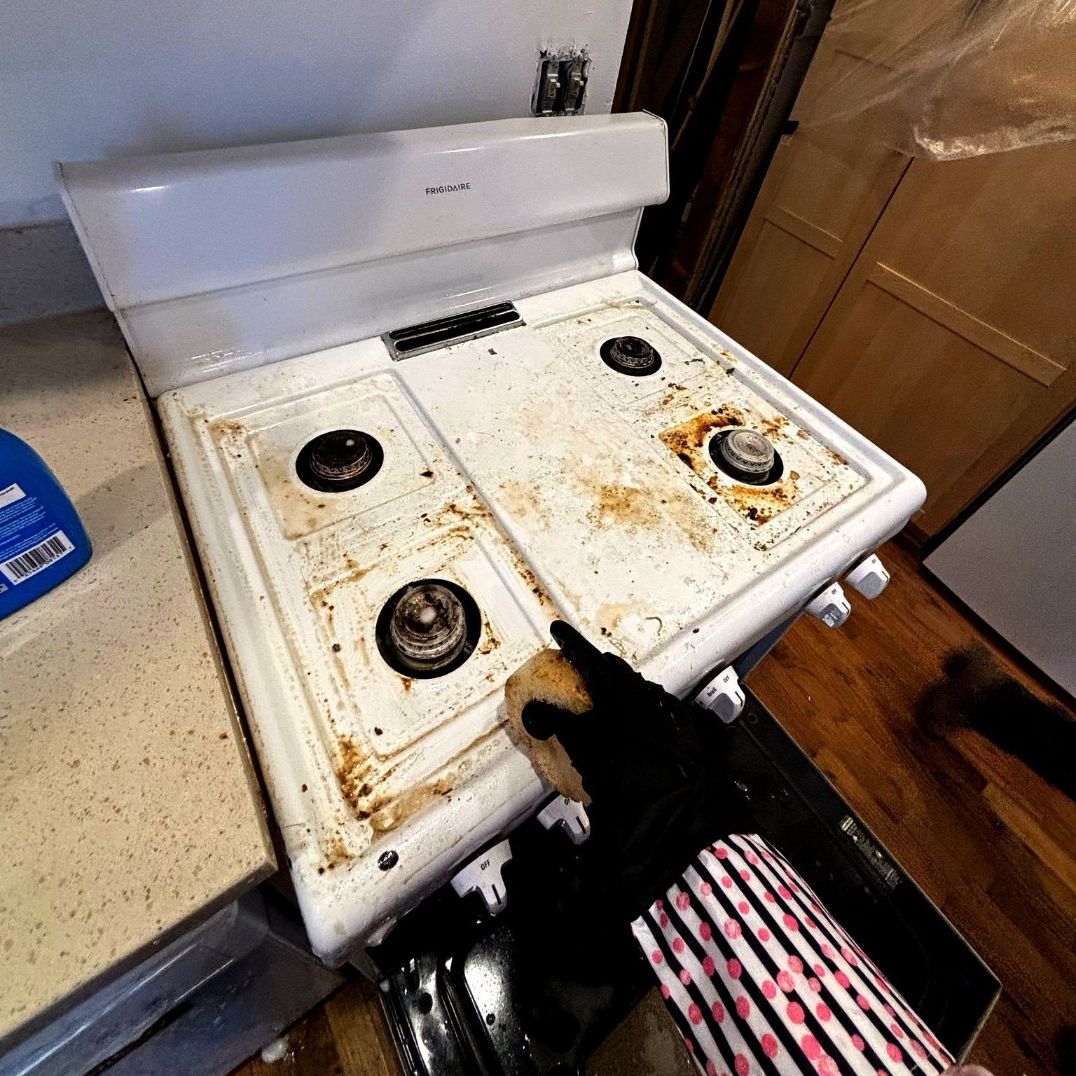 A person is cleaning a dirty stove top with a brush