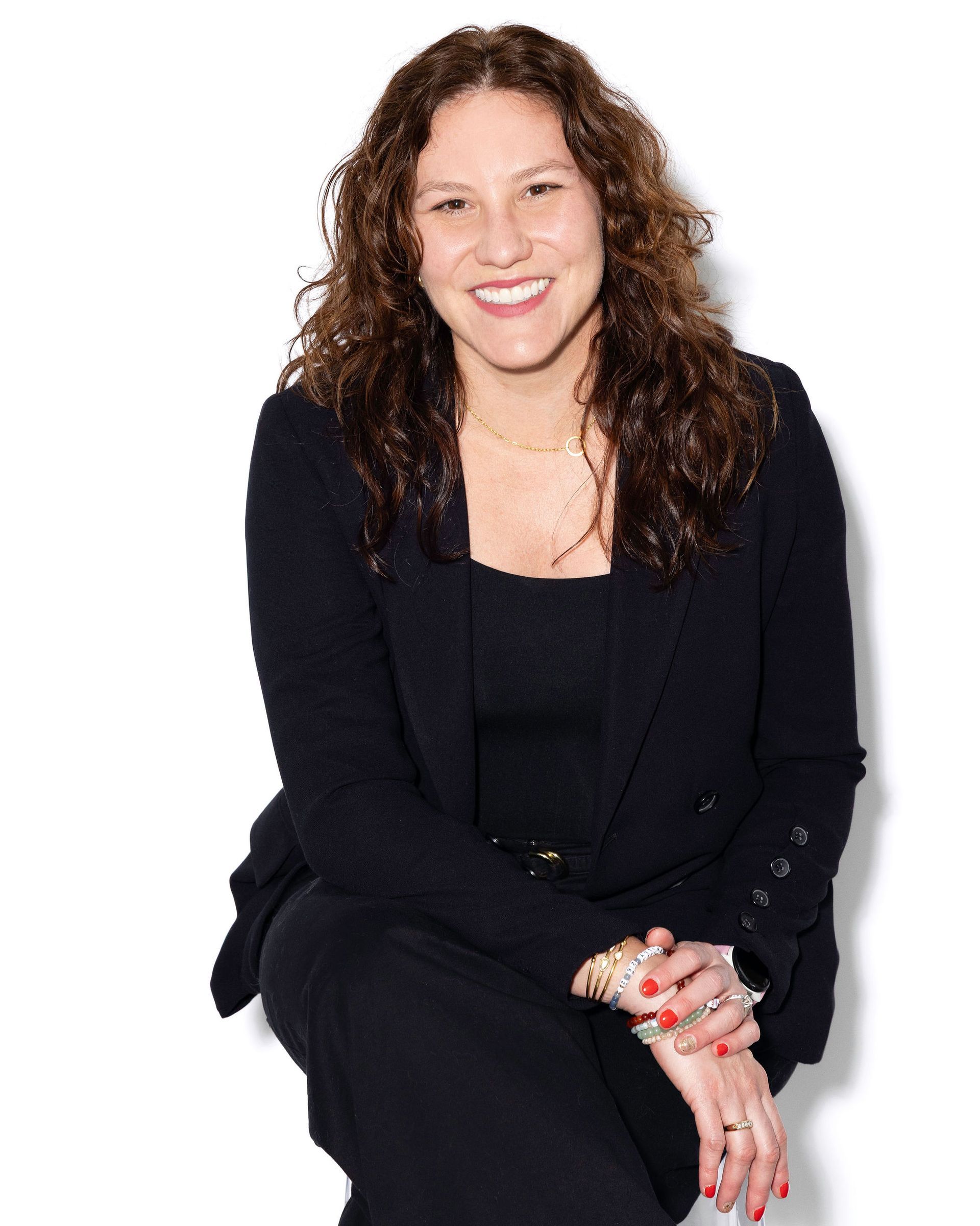 Woman with glasses smiles; wearing a white shirt against a dark background.