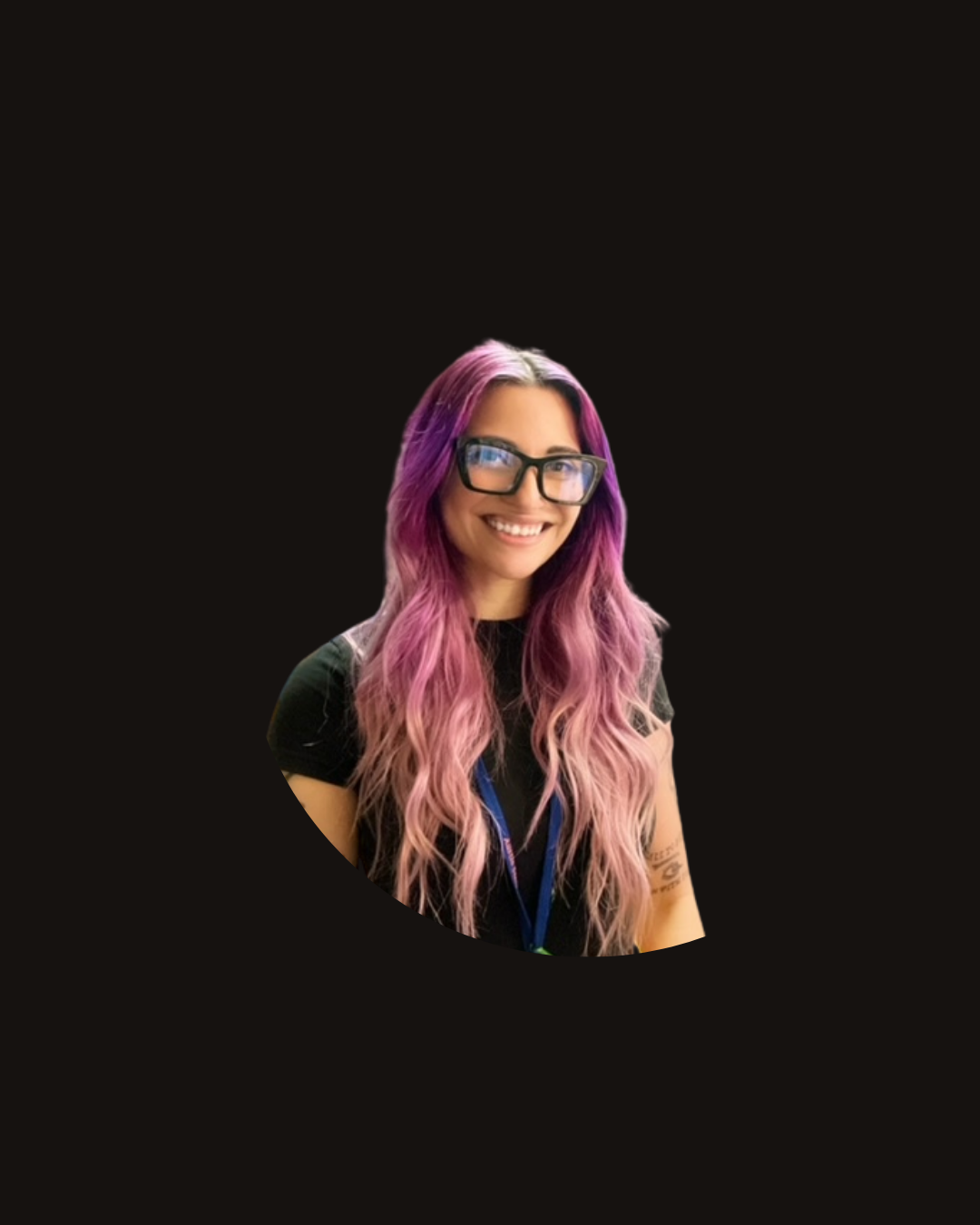 Woman with purple and pink hair, glasses, and a black shirt smiling in a library.