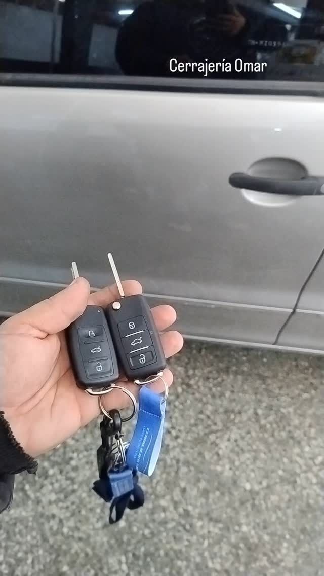 Persona sosteniendo dos llaves de coche, puerta de coche con manija al fondo.