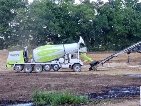 Concrete mixer truck pouring concrete onto a conveyor belt at a construction site.