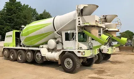 Two concrete mixer trucks, white and lime green, parked on pavement, outdoors.