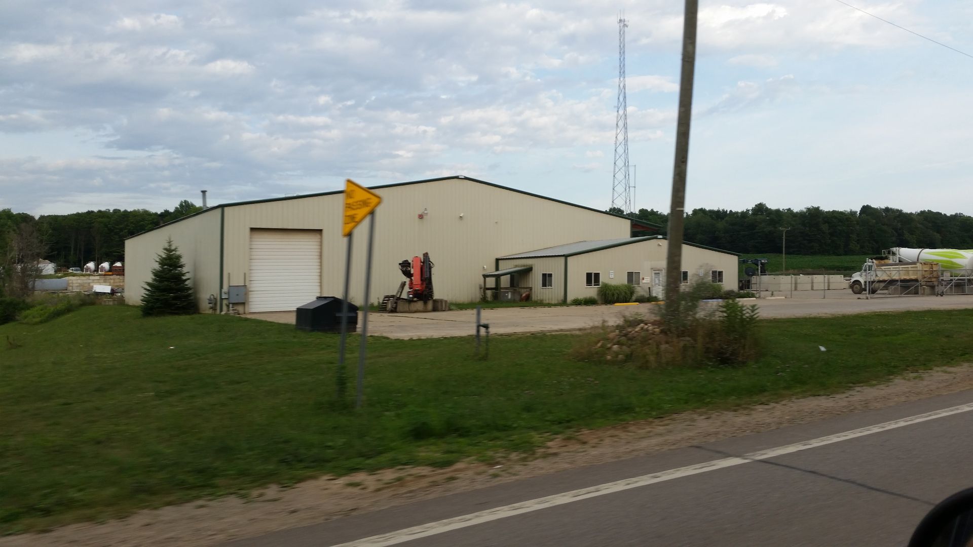 Warehouse with white garage door, yellow sign, tall antenna in background, cloudy sky.