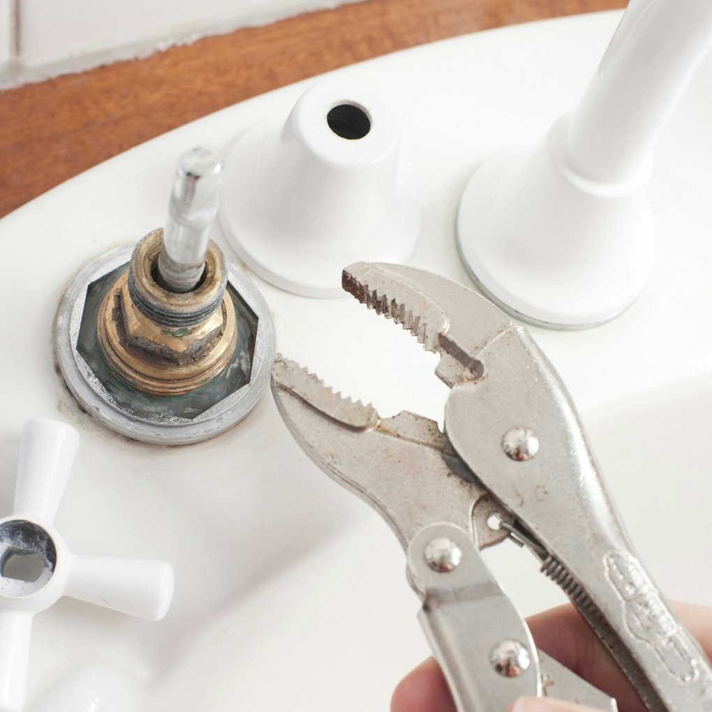 A person is holding a pair of pliers in front of a sink