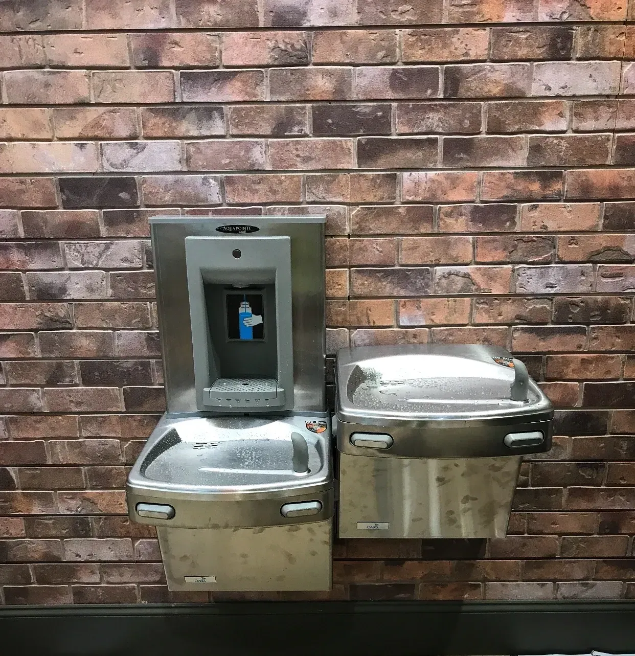 A brick wall with two stainless steel fountains on it