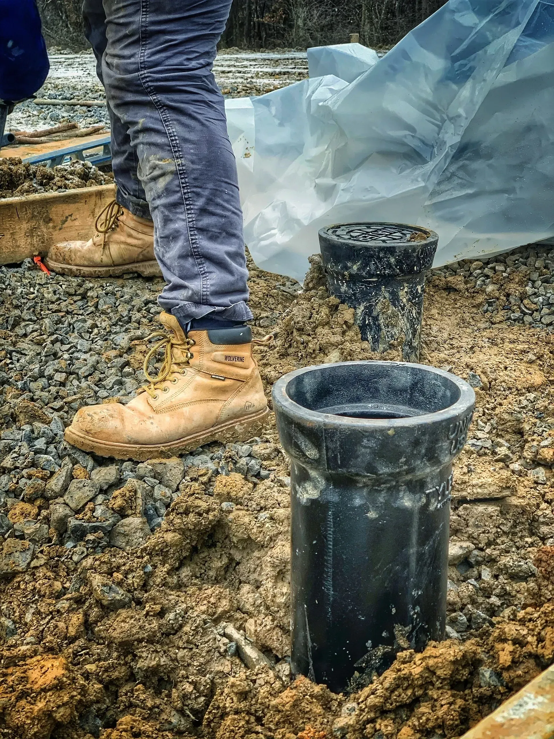 A person is standing next to a pipe in the dirt.