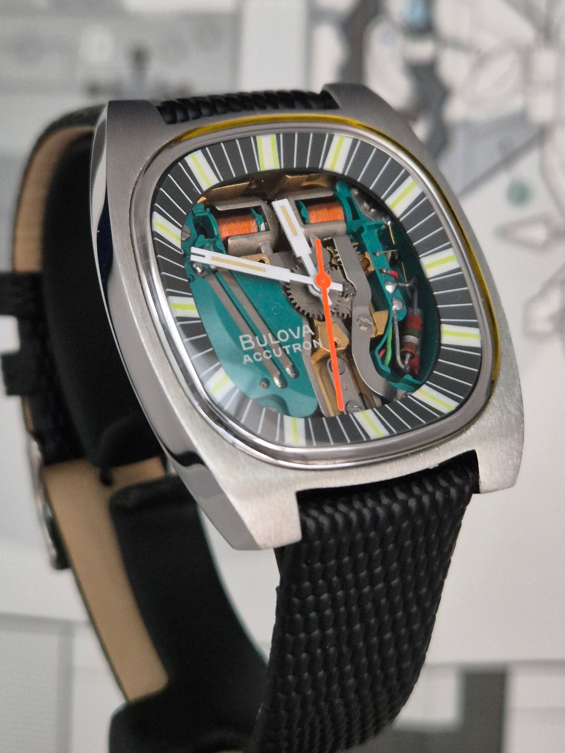 Bulova Accutron watch with open dial, showing inner workings. Black strap, silver case, green, orange, and white details.