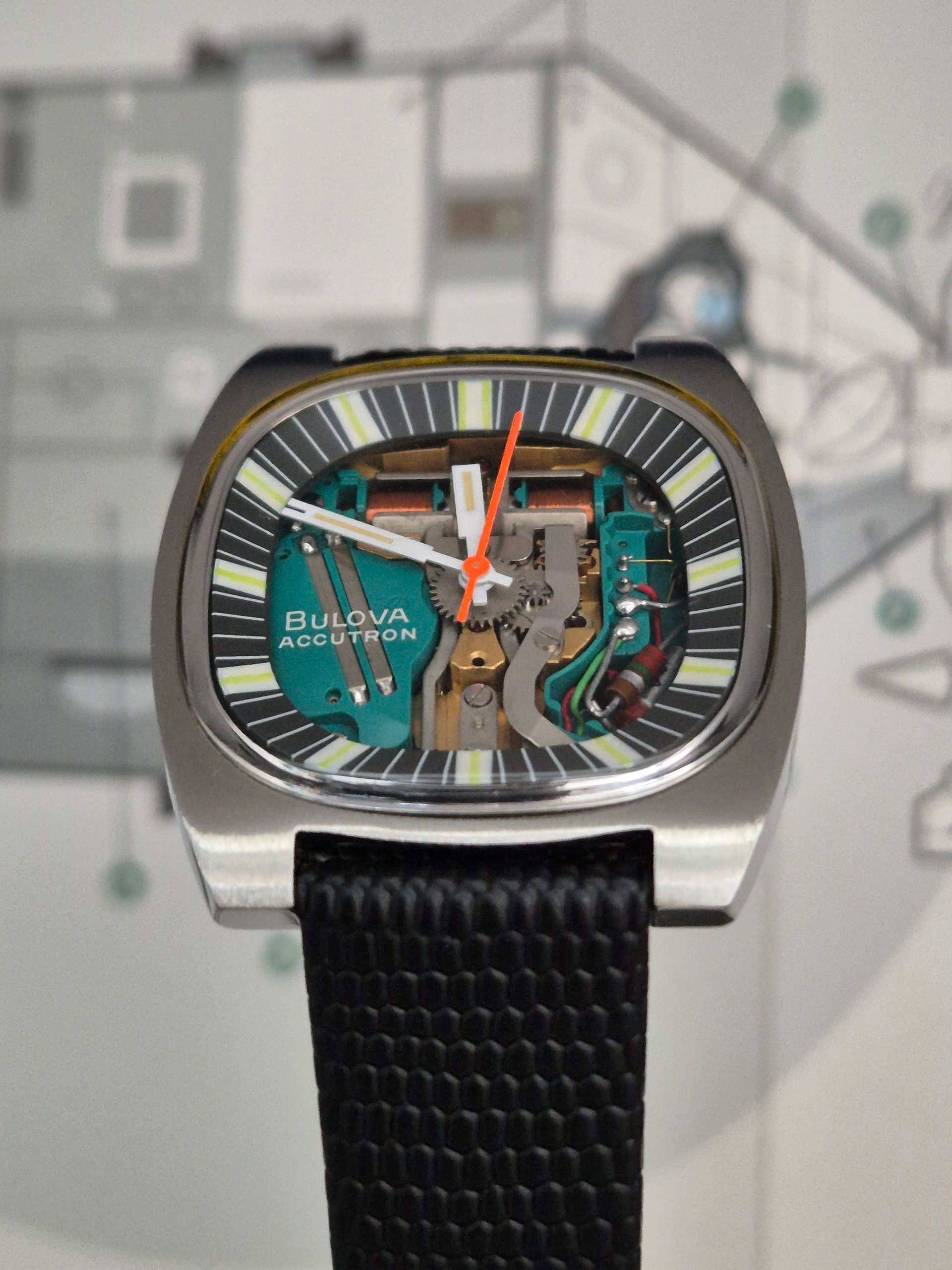Bulova Accutron watch with exposed movement, teal accents, orange second hand, black strap.