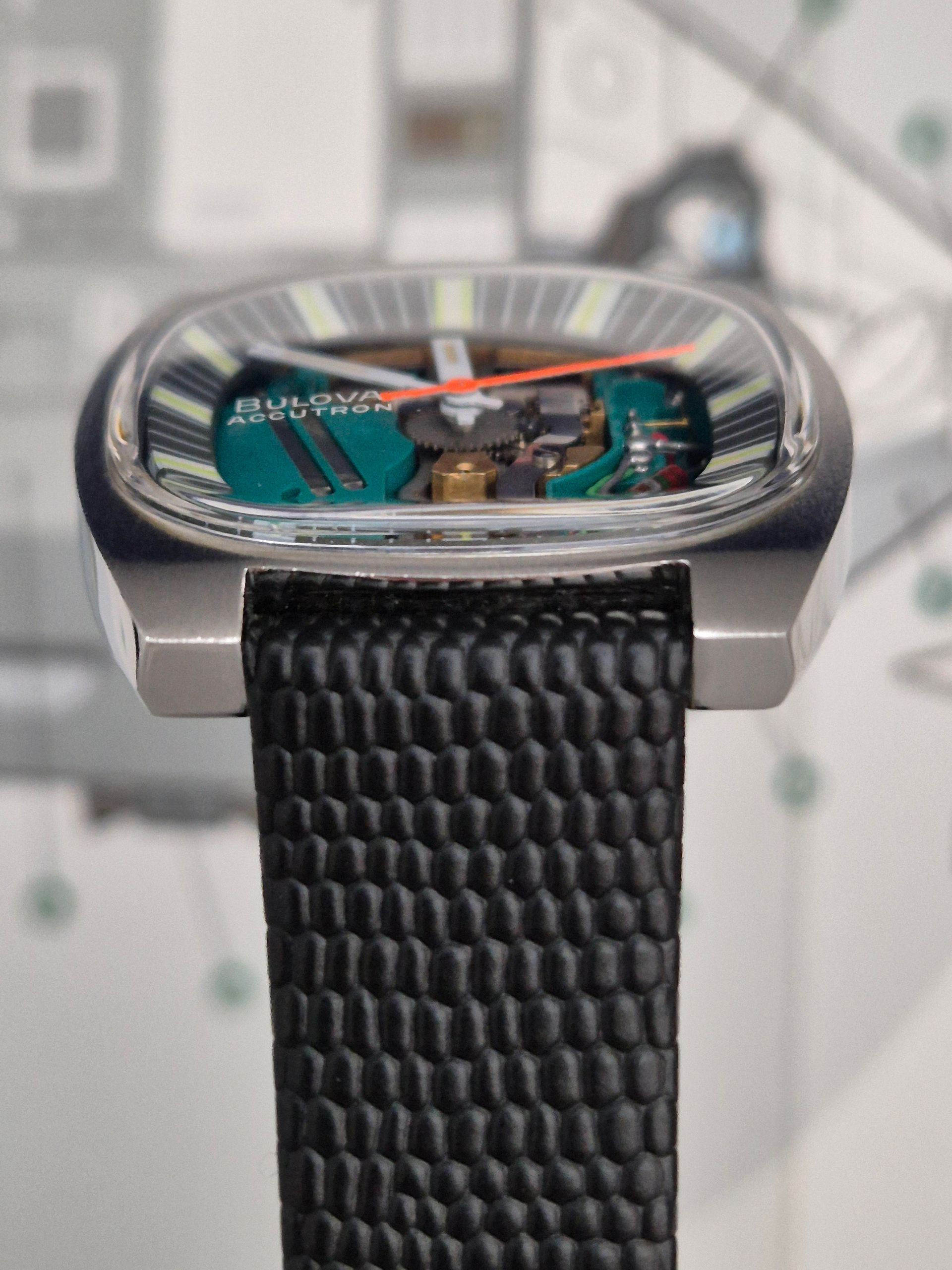 Side view of a Bulova watch with a clear face, black strap, and visible internal components.