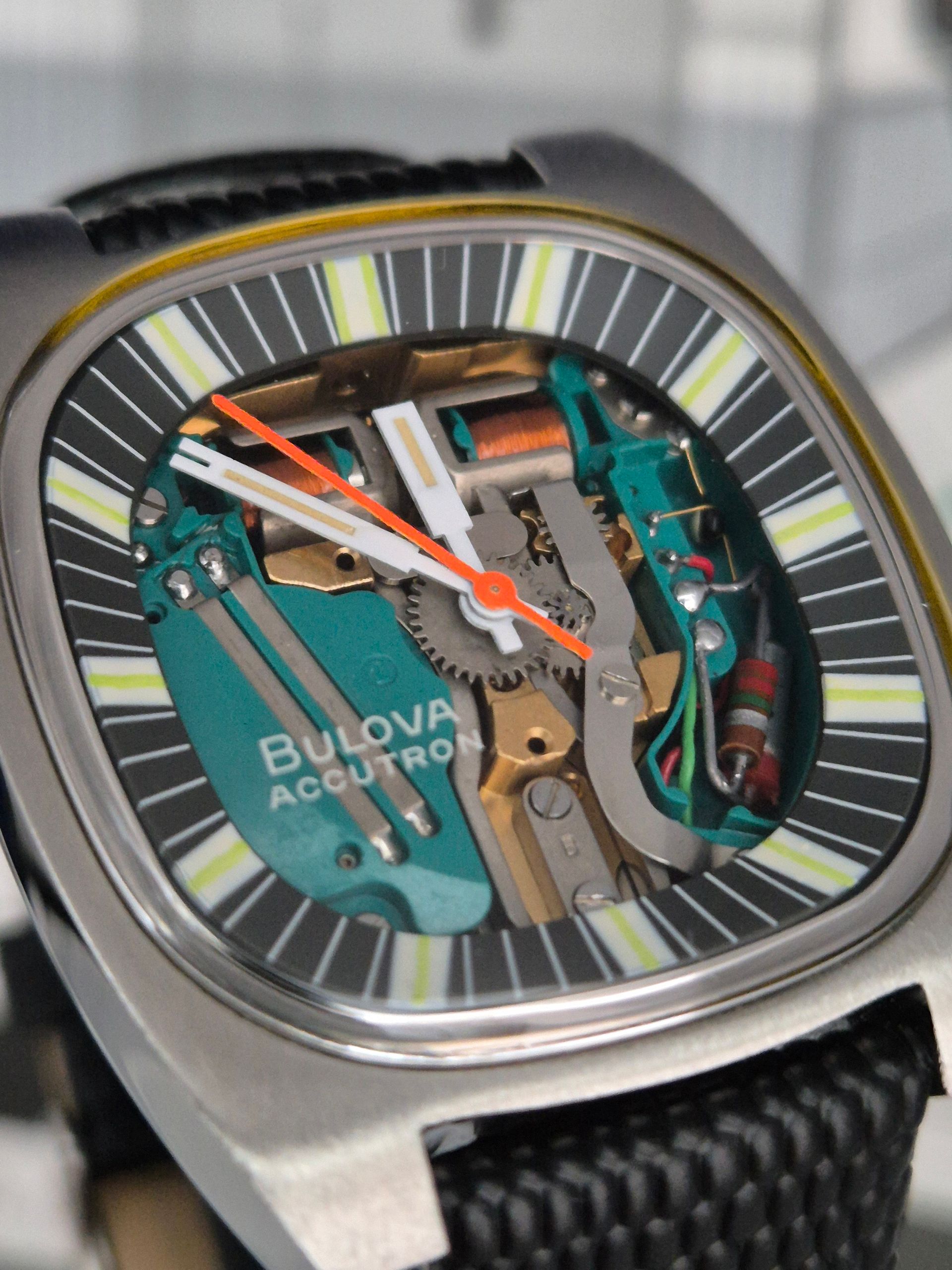 Bulova Accutron watch with open face, showcasing teal and gold internal mechanics, with an orange second hand.