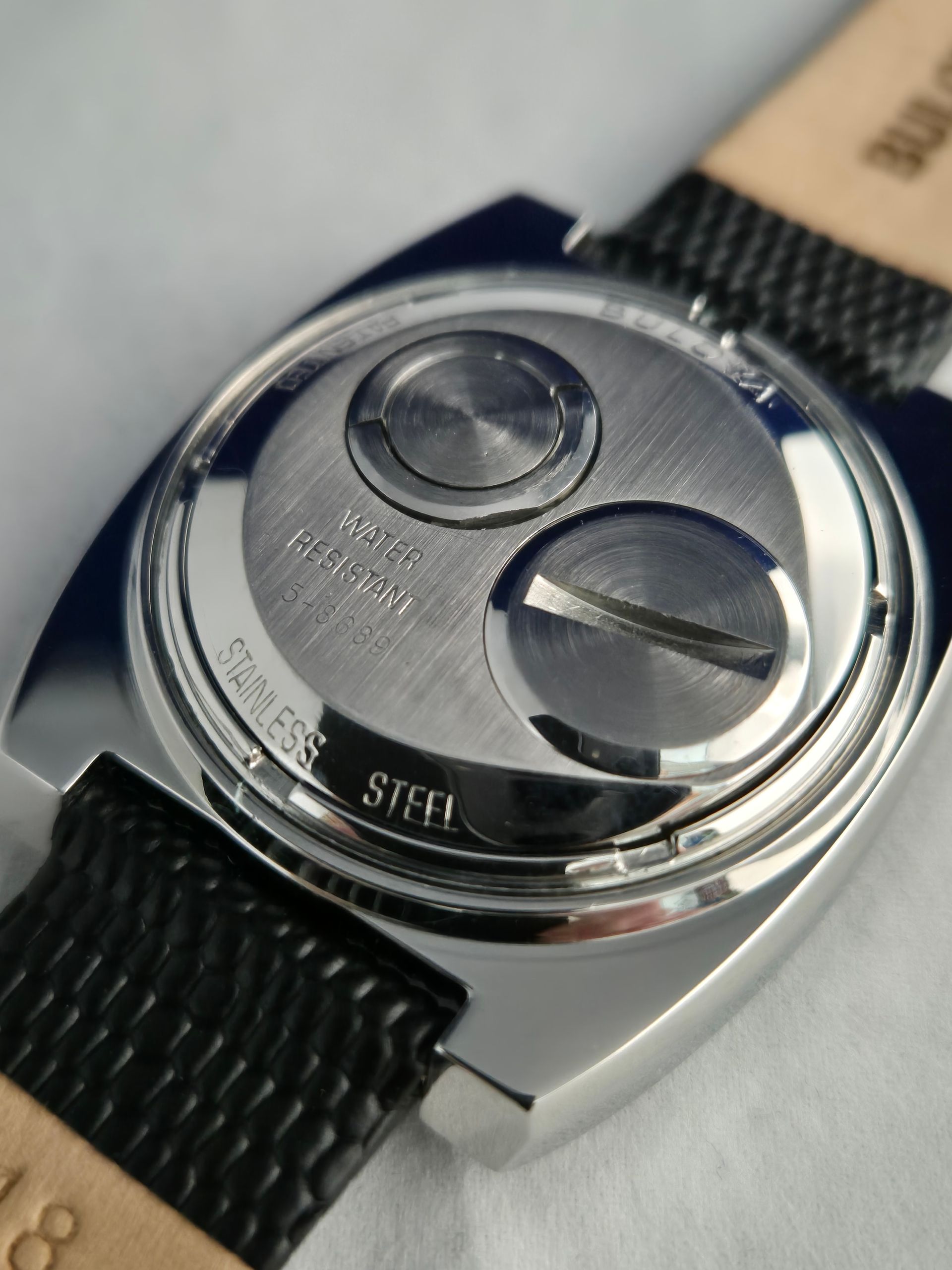 Back of a stainless steel watch with two circular compartments, text