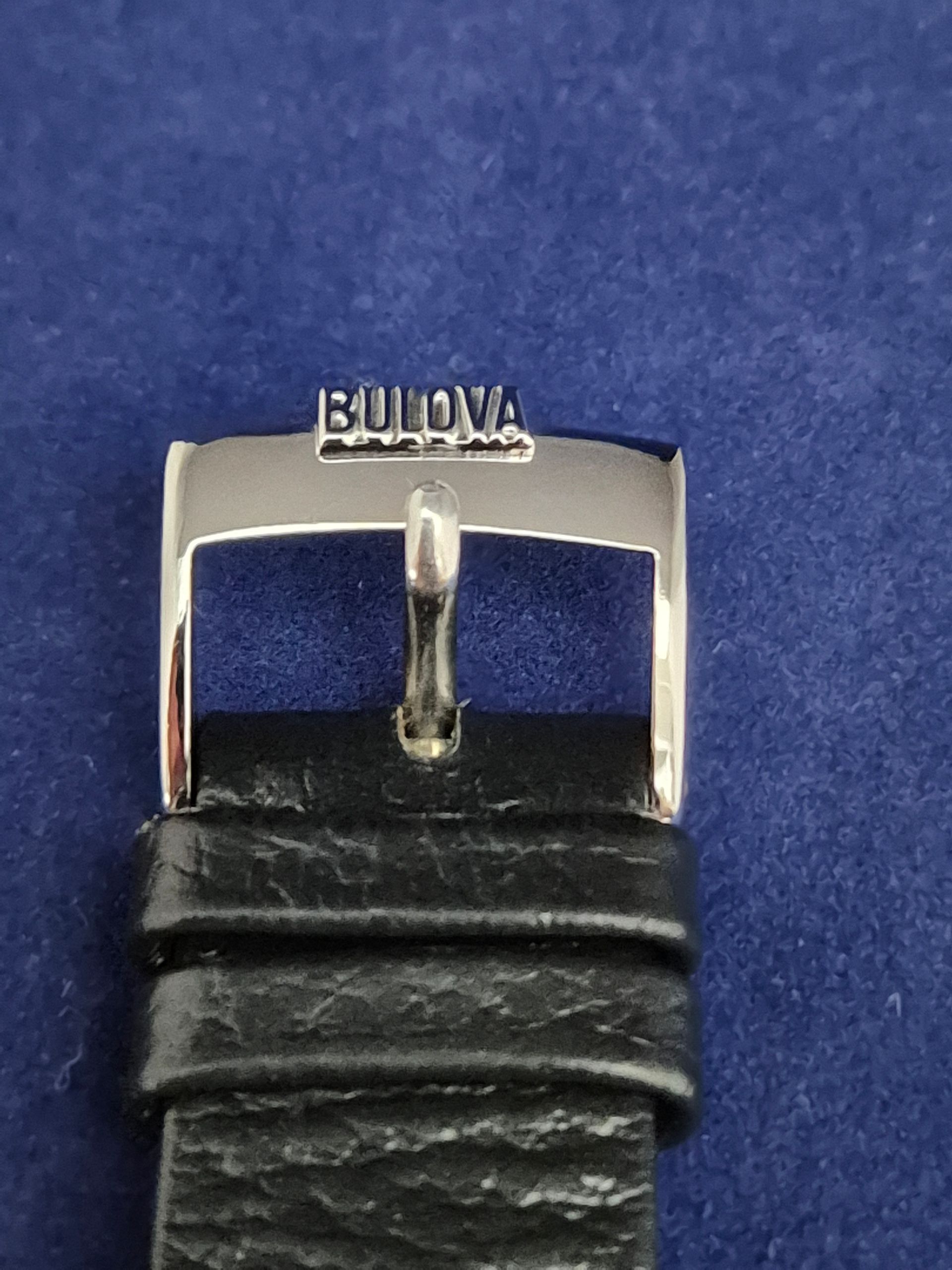 Silver Bulova watch buckle on black leather strap.