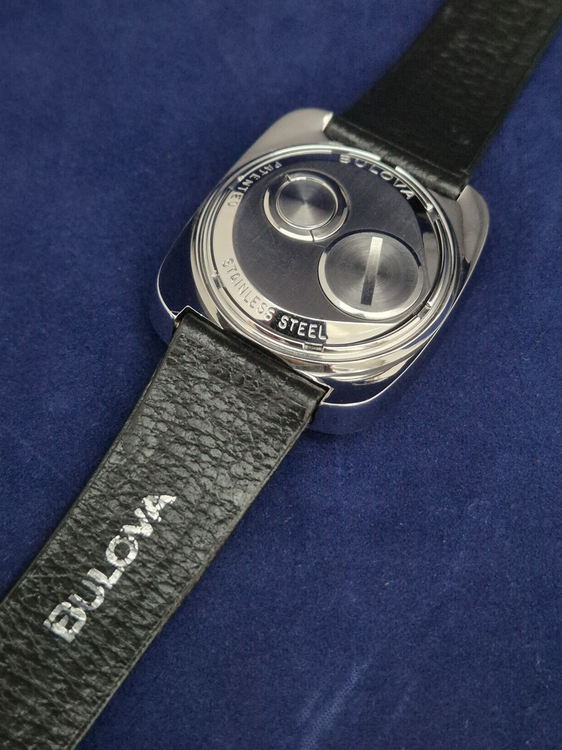 Back of a Bulova watch with black leather strap, stainless steel case, and two round mechanisms.