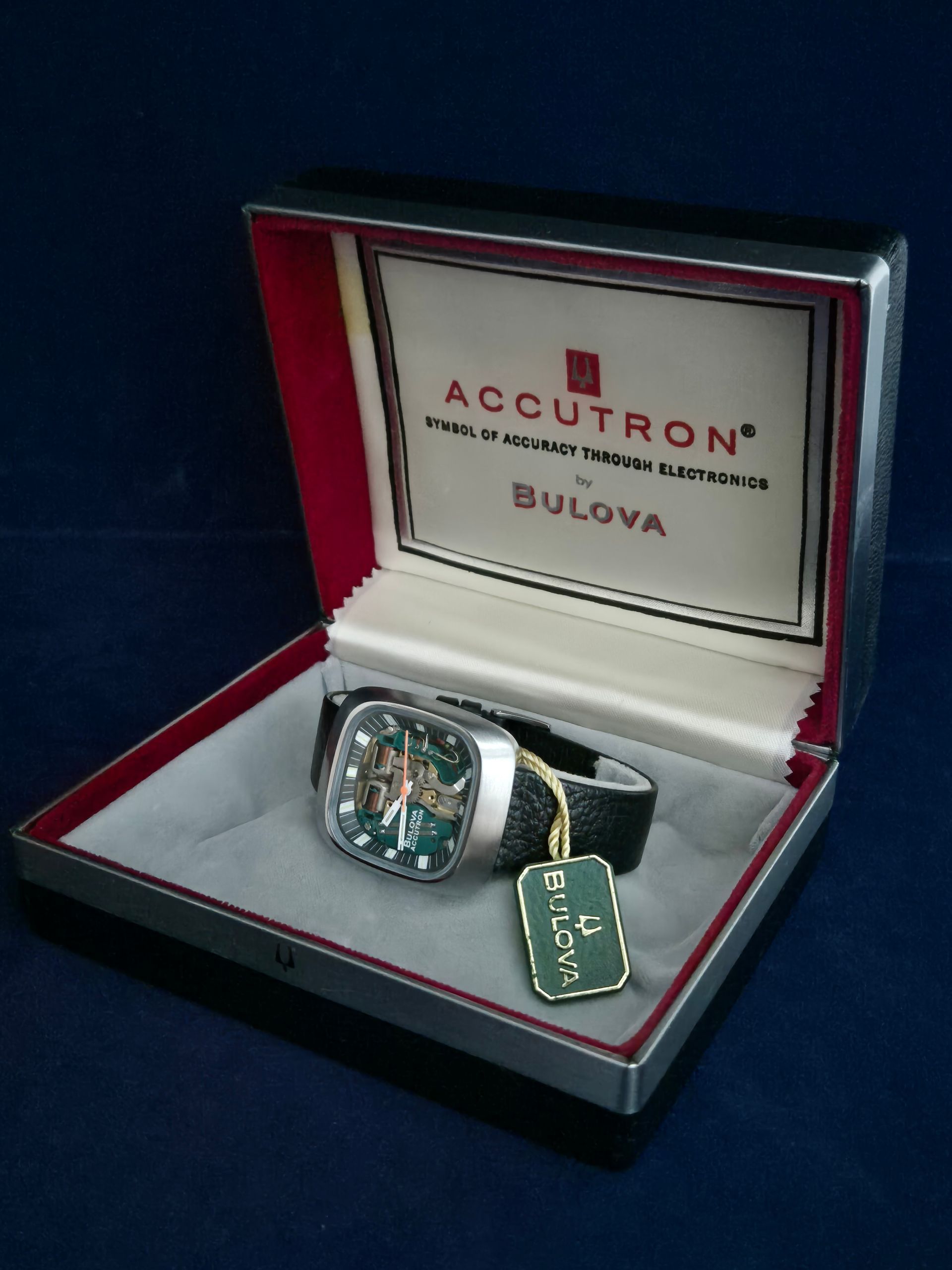 Bulova Accutron watch in its box; silver case, green dial, black strap, with tag.