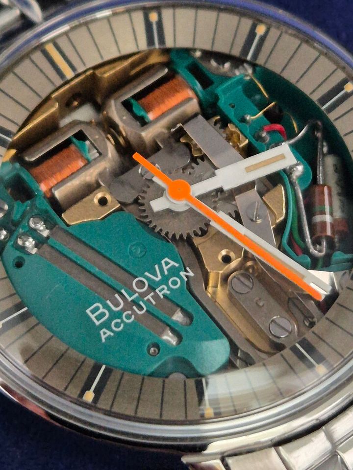 Close-up of a Bovan Accutron watch face with orange hands and teal internal mechanism
