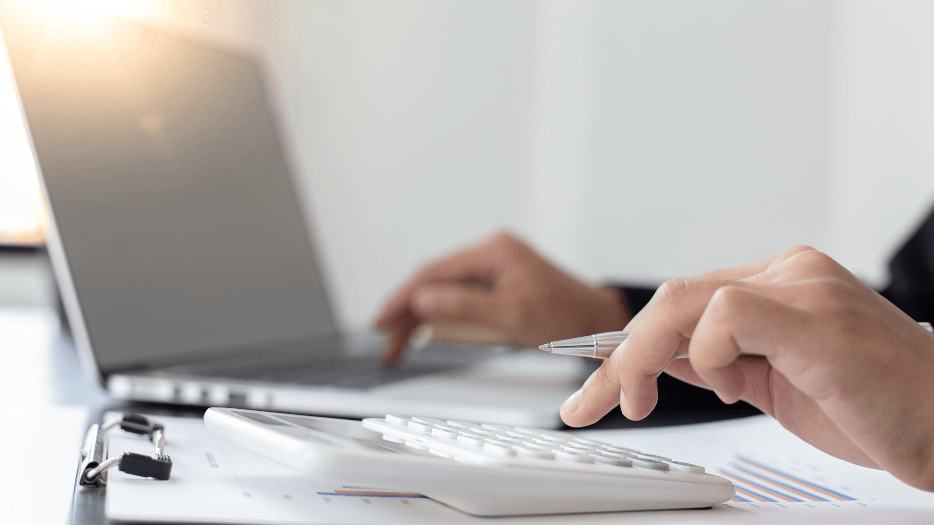 A person is using a calculator in front of a laptop computer.