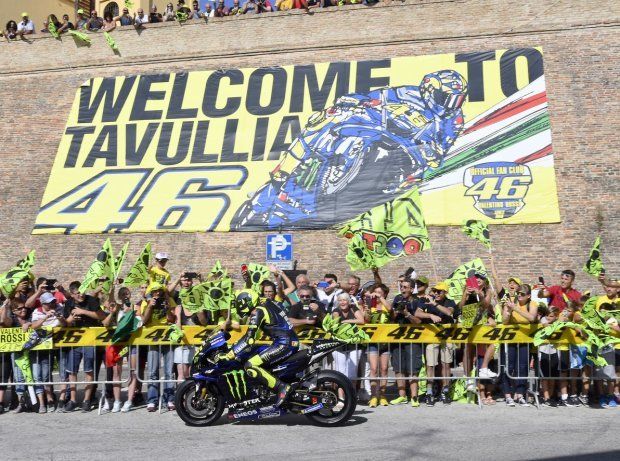 Motorrijder Valentino Rossi op een Yamaha-motor wordt begroet door juichende fans in Tavullia, Italië, onder de banner 